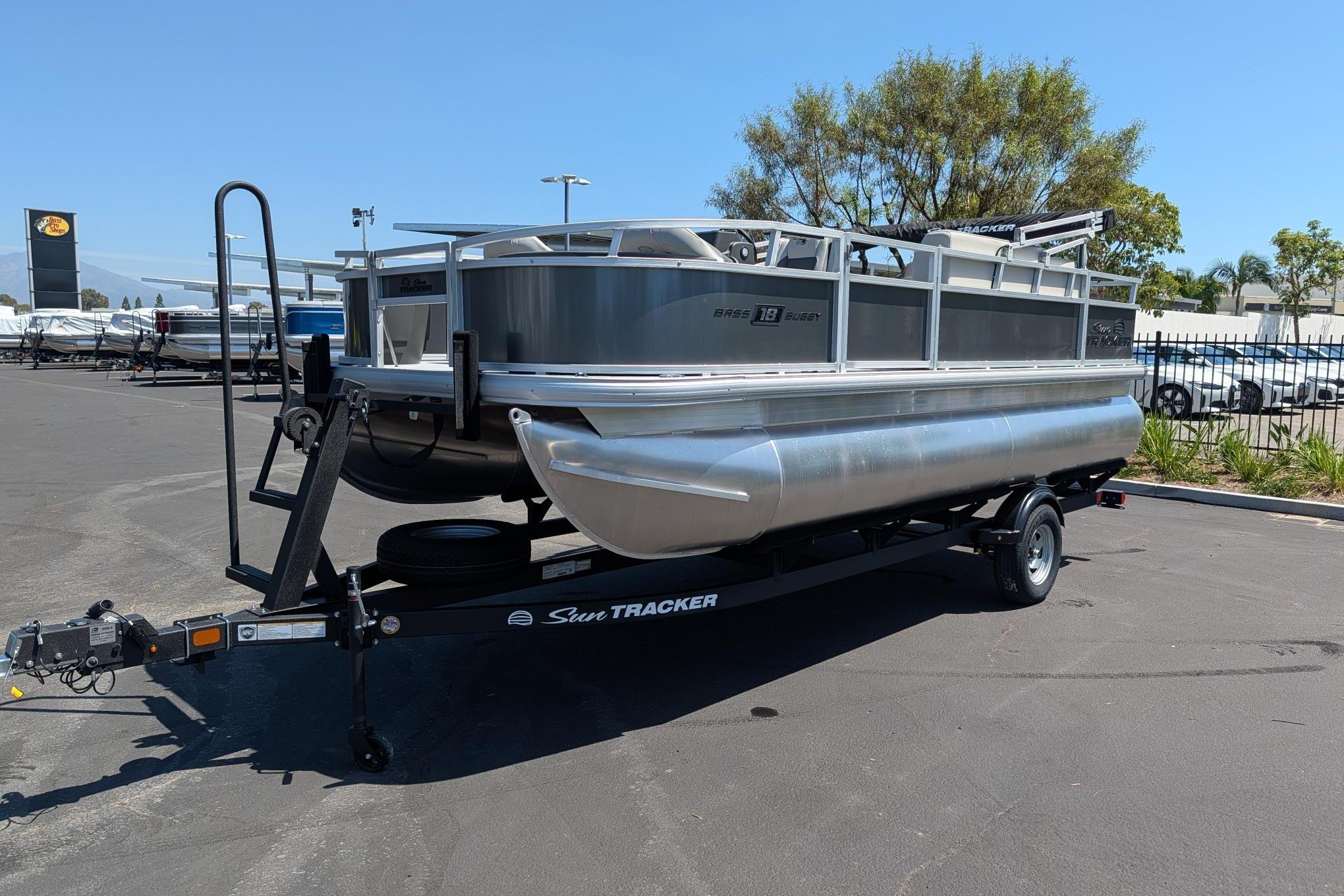2026 Sun Tracker Bass Buggy 18 DLX pontoon boat on trailer in parking lot.