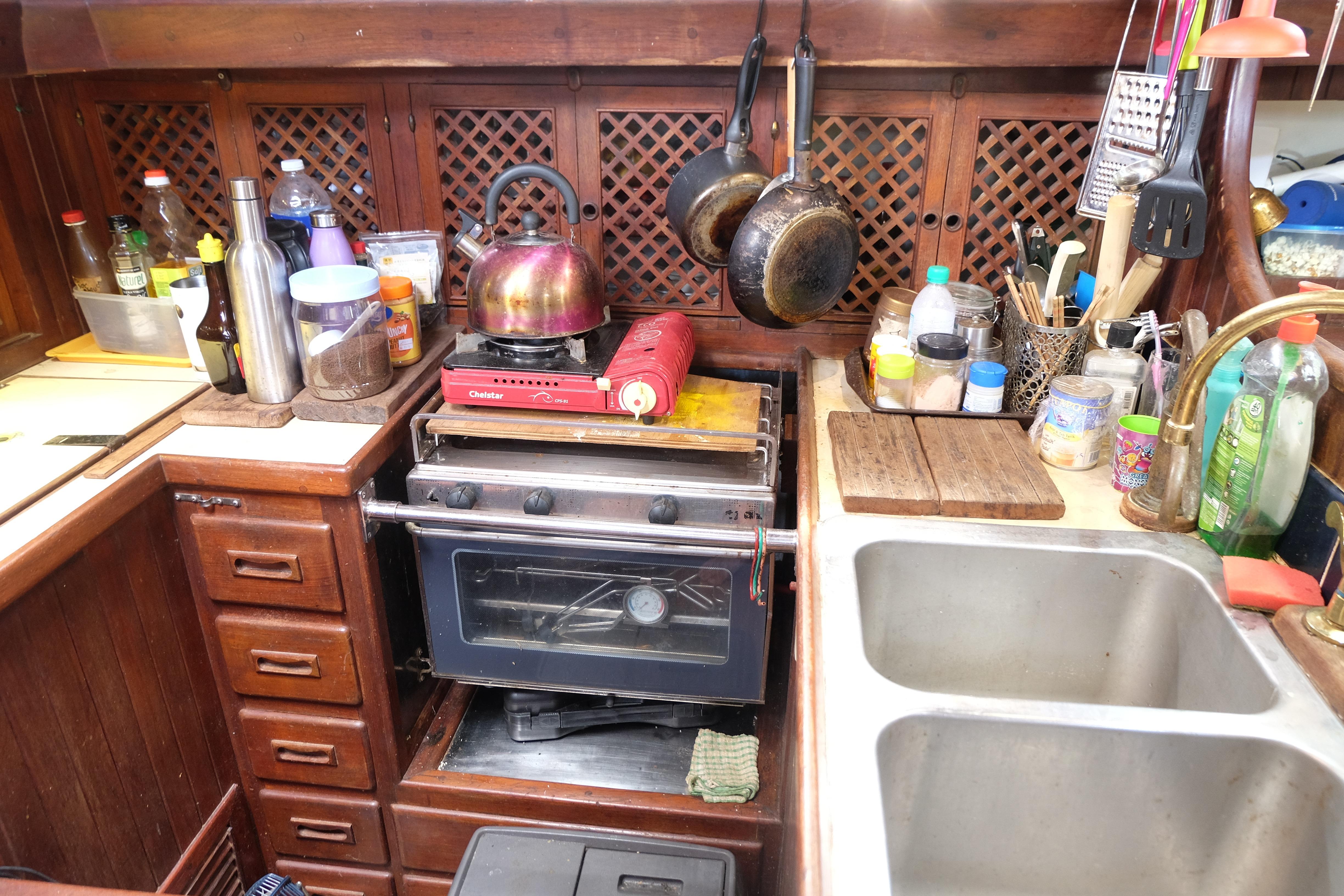 Cozy 1979 Westwind 35 boat kitchen with stove, sink, and hanging pans.