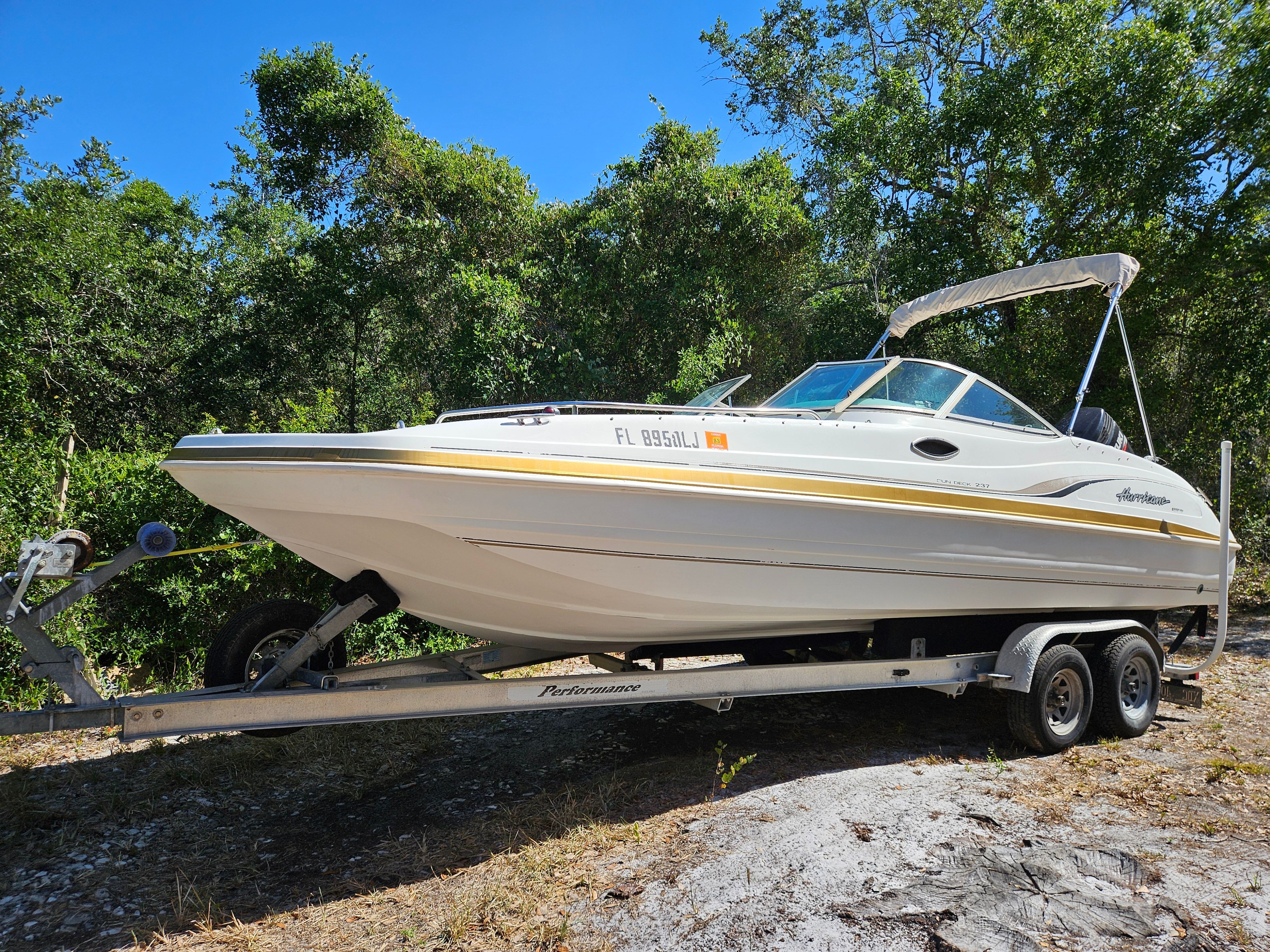 A 2001 Hurricane 237 boat on a trailer, surrounded by trees.
