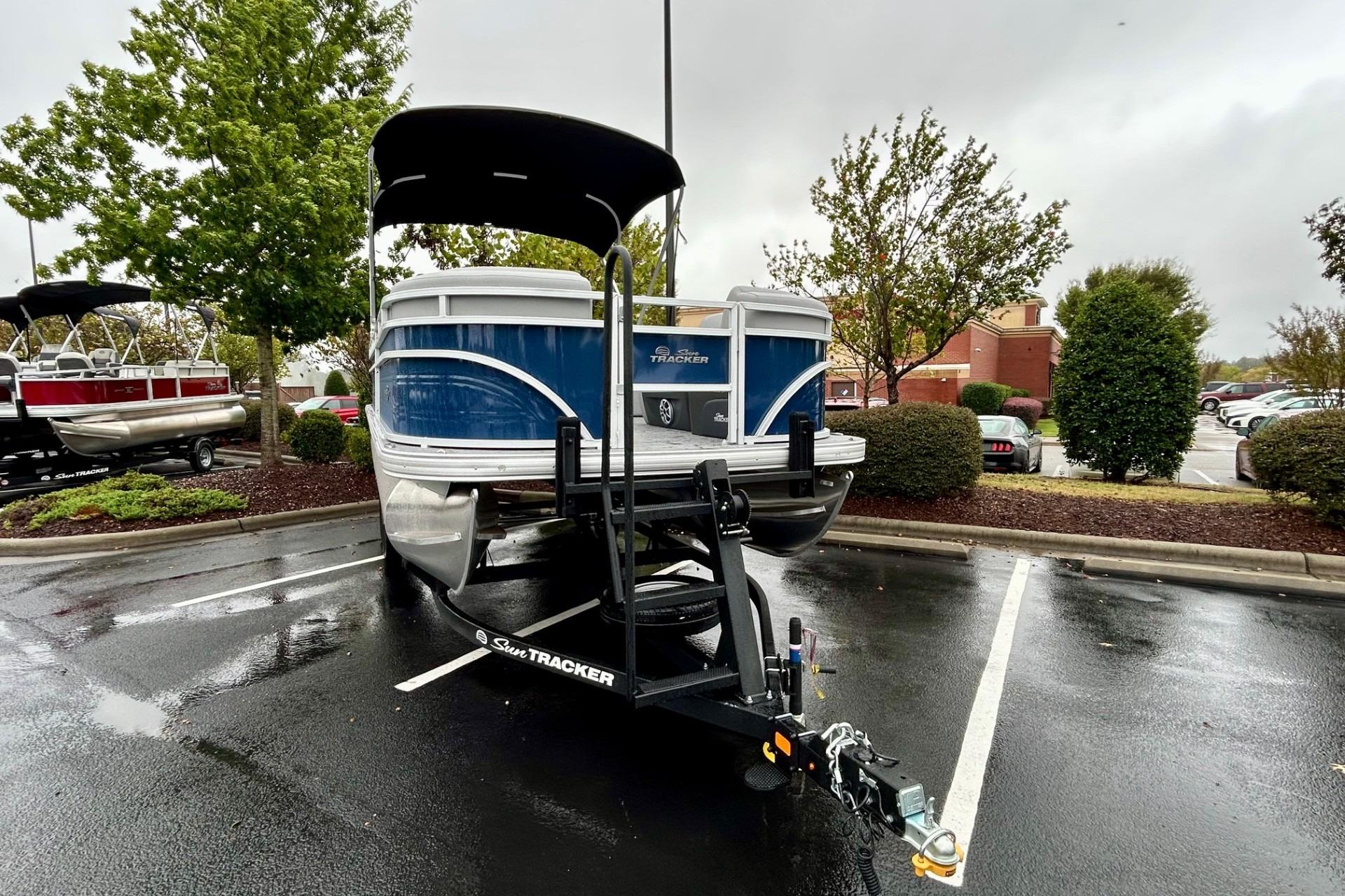 2026 Sun Tracker SportFish 22 DLX pontoon boat on trailer in parking lot.
