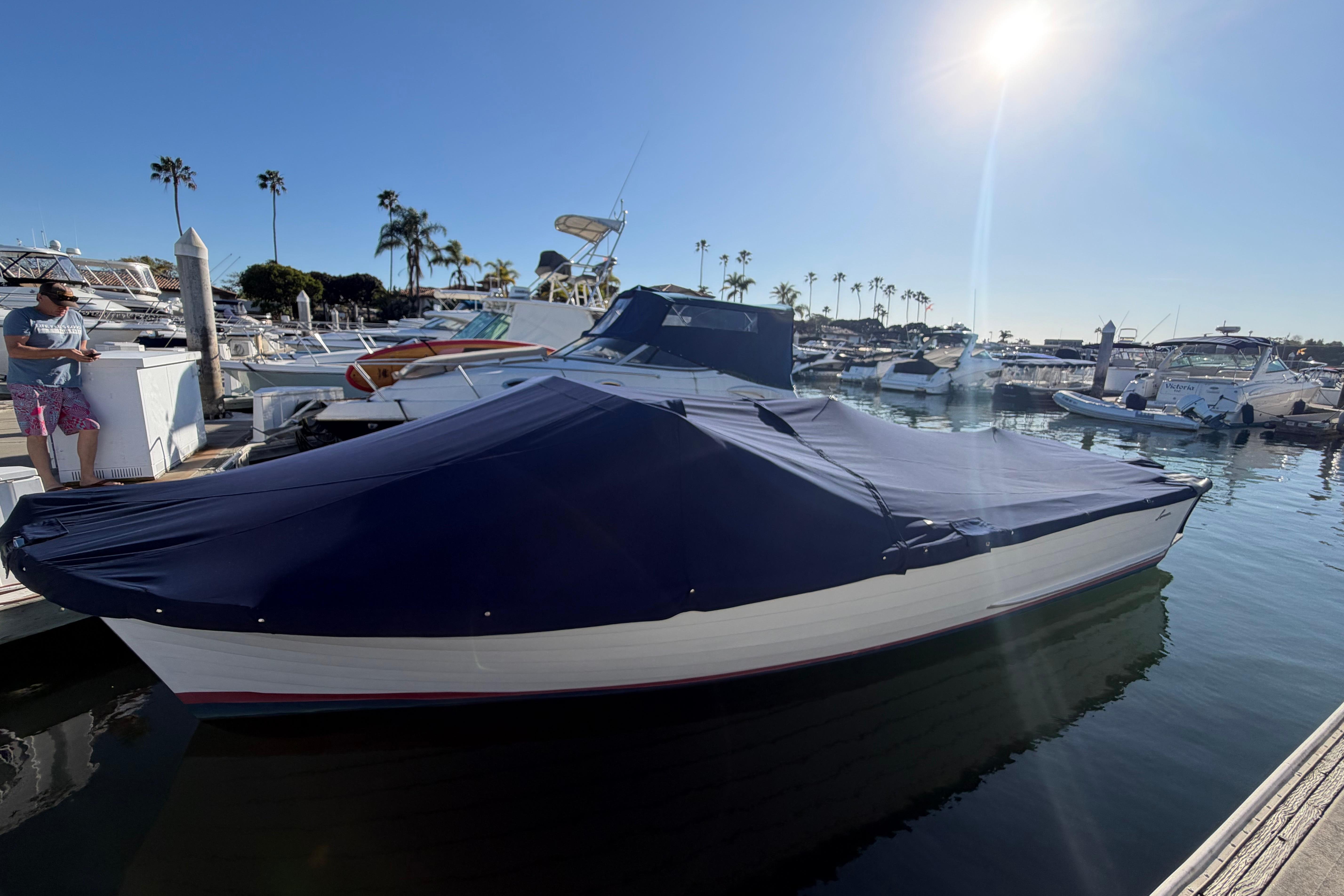 1964 Lyman 25 Sleeper boat covered at marina under clear blue sky.