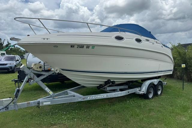 2004 Sea Ray 240 Sundancer boat on trailer, parked on grass under cloudy sky.