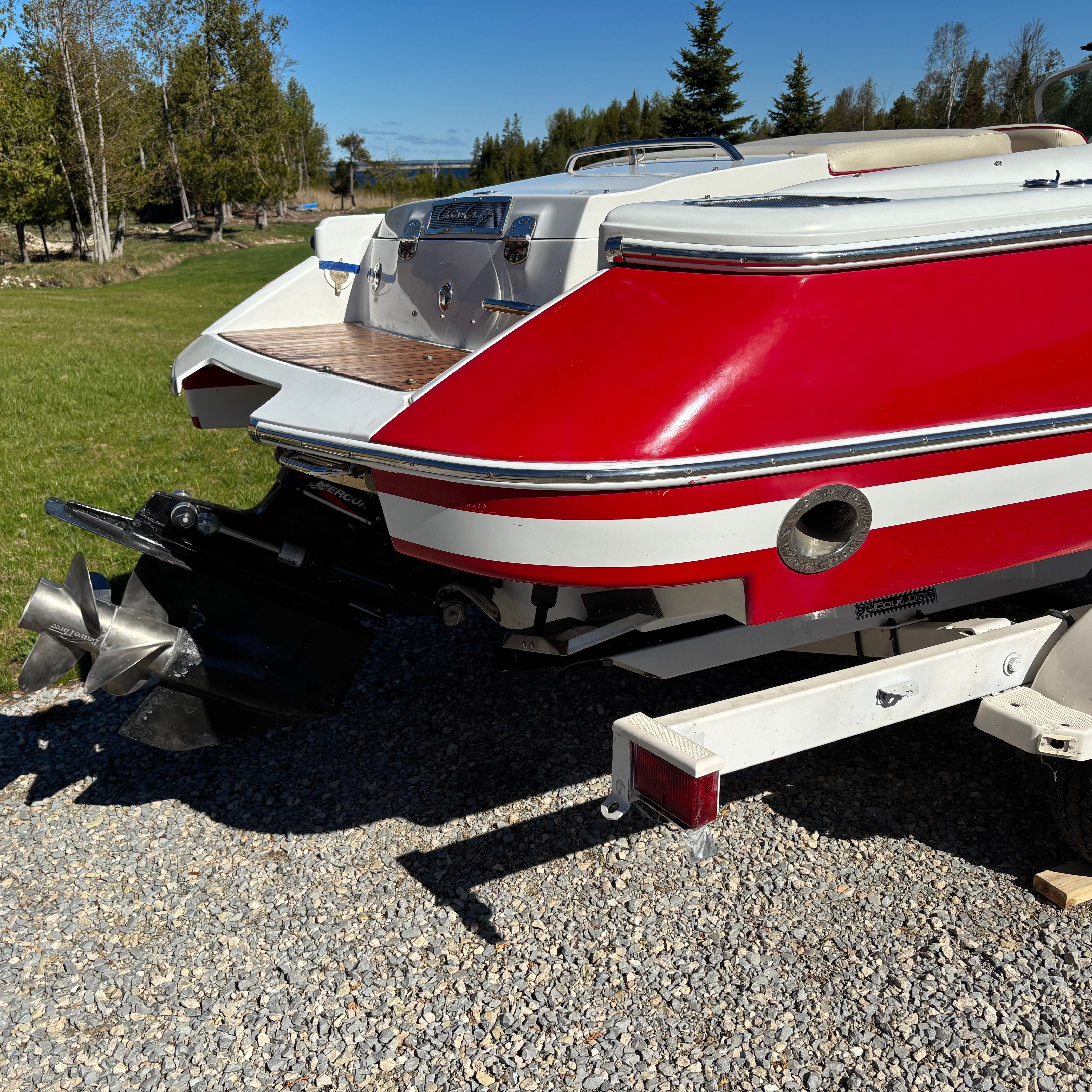 Red Chris-Craft Launch 22 boat from 2003 on a trailer, surrounded by trees and grass.