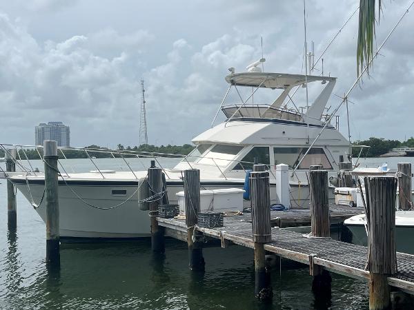 1985 Hatteras 45 Convertible yacht docked at marina under cloudy sky.
