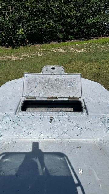 A boat with an open storage compartment on grass, surrounded by trees.