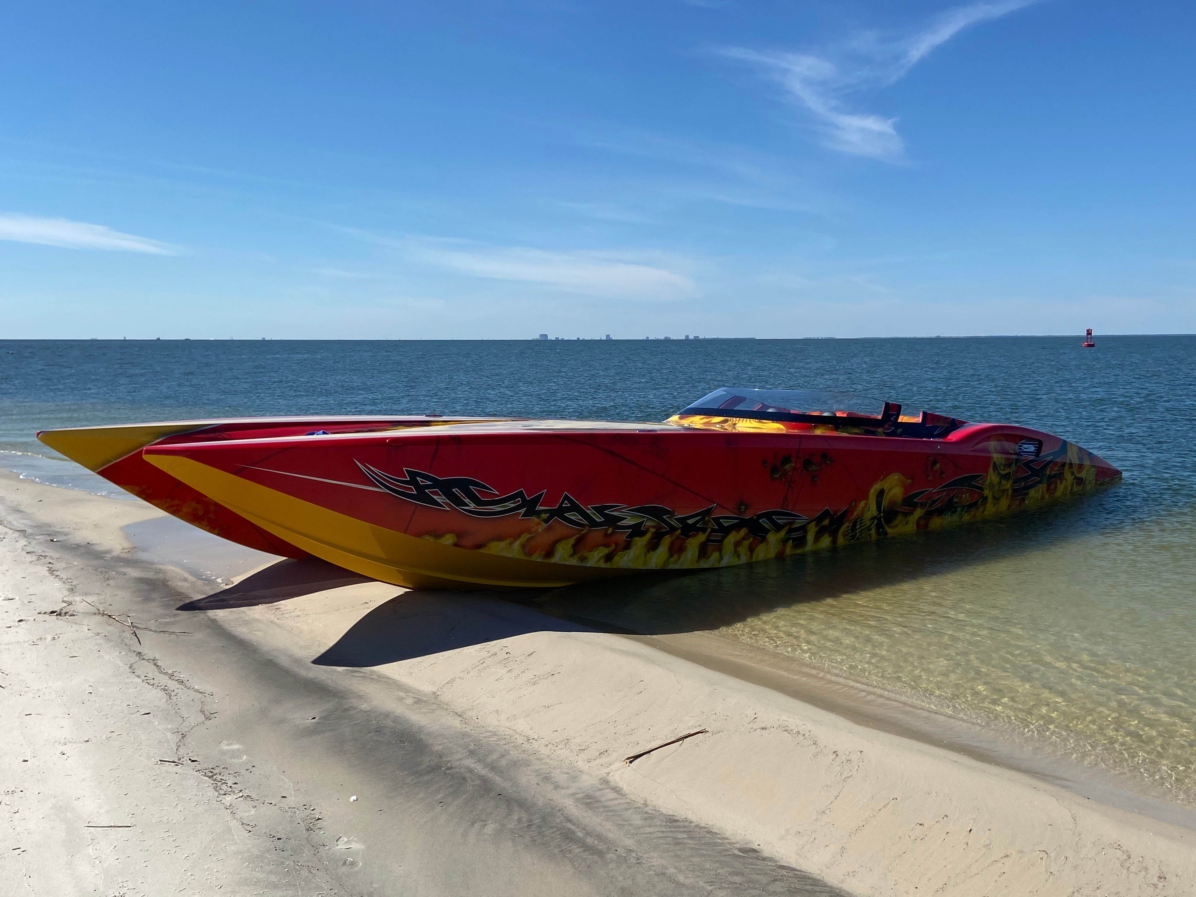 A 2010 MTI CAT with striking, colorful design rests on the sandy shore of a calm water body.