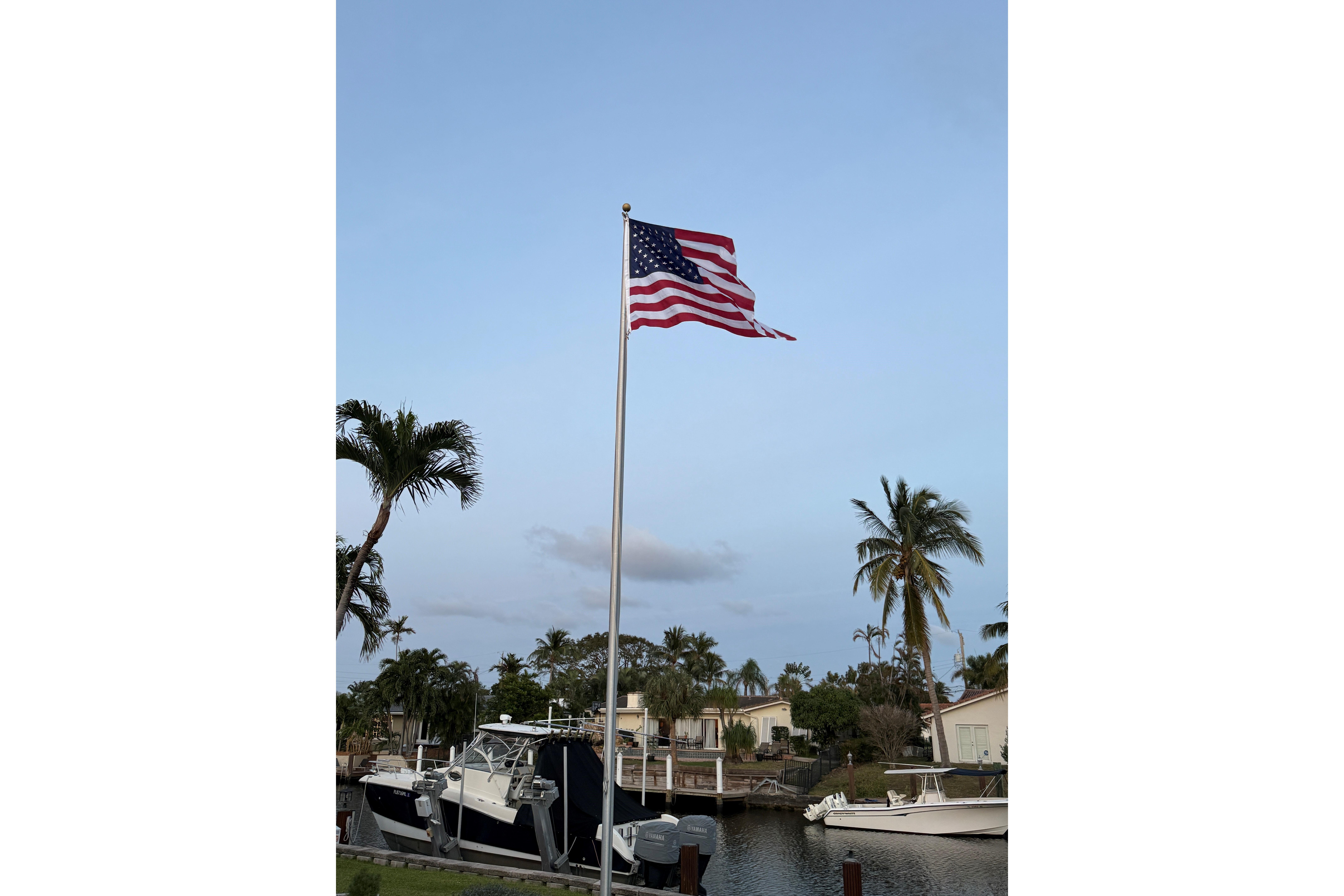 American flag waving near a 2003 World Cat 270 EC boat, surrounded by palm trees.