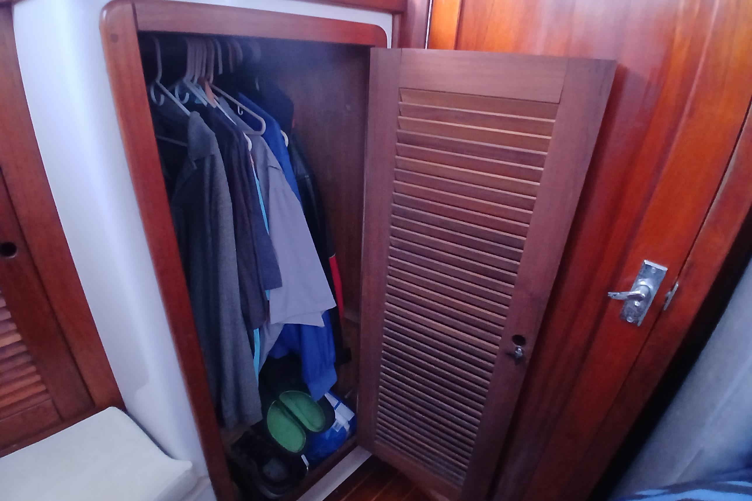 Wooden closet with clothes and shoes inside a 1995 Catalina 42 MkII sailboat.