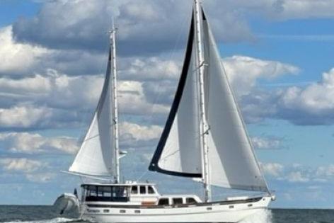 1980 Cheoy Lee 52 Motorsailer sailing under blue skies with white clouds.
