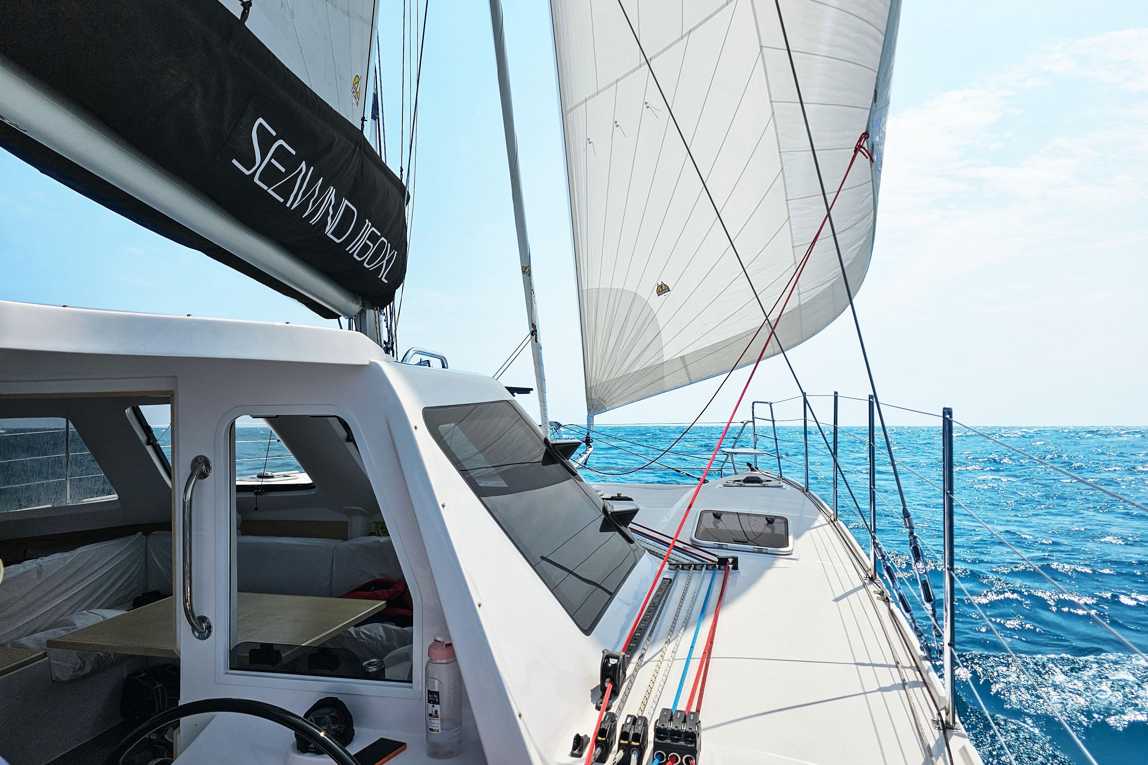 Sailing on a 2026 Seawind 1160XL catamaran, gliding smoothly over clear blue ocean waters.