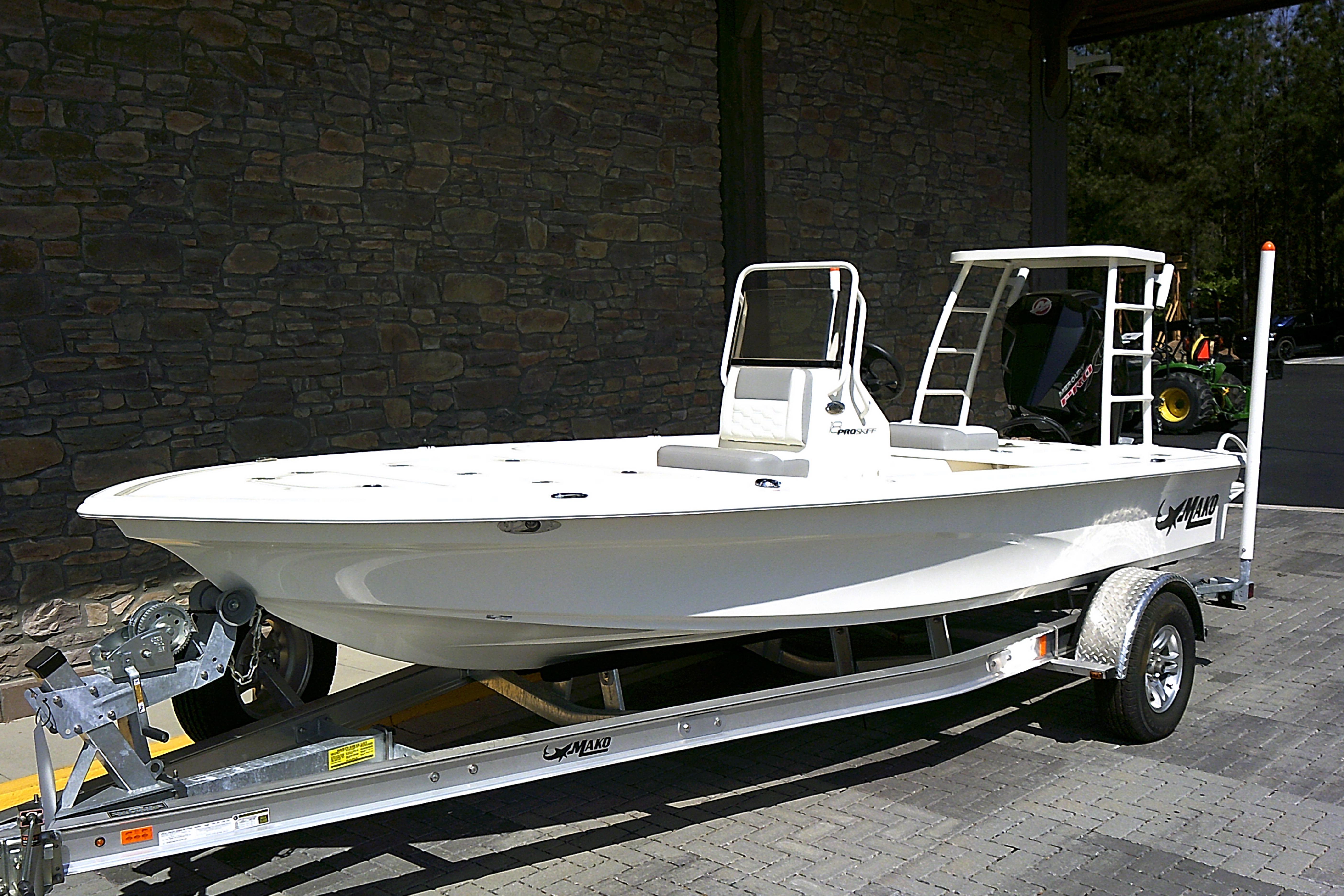 2026 Mako 18 Pro Skiff boat on trailer, parked outdoors against stone wall.