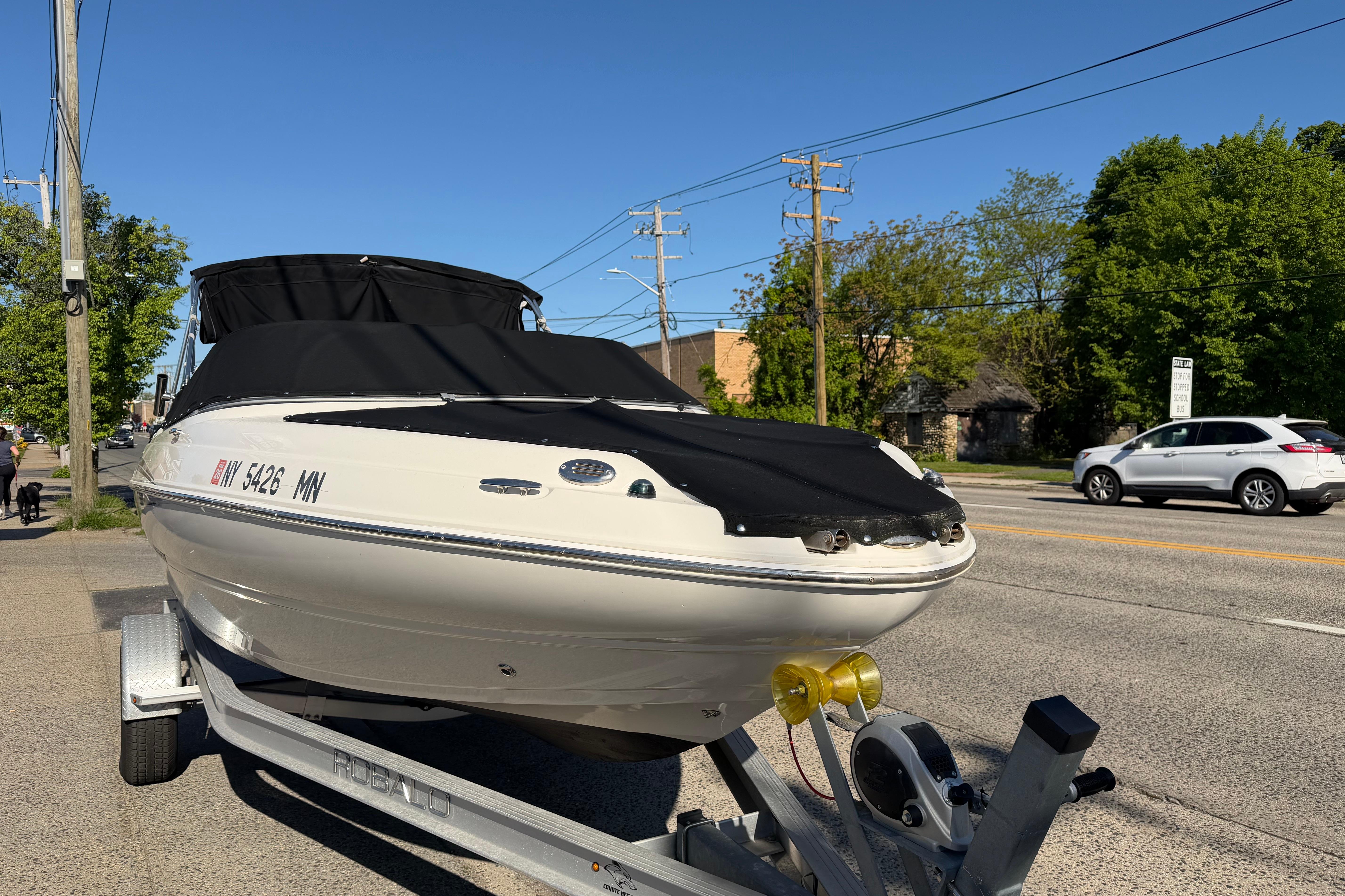 2018 Stingray 204 LR boat on trailer, covered, parked roadside under clear blue sky.