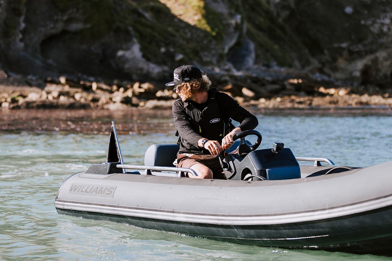 Man steering Williams Jet Tenders Sportjet 395 on water near rocky shore.