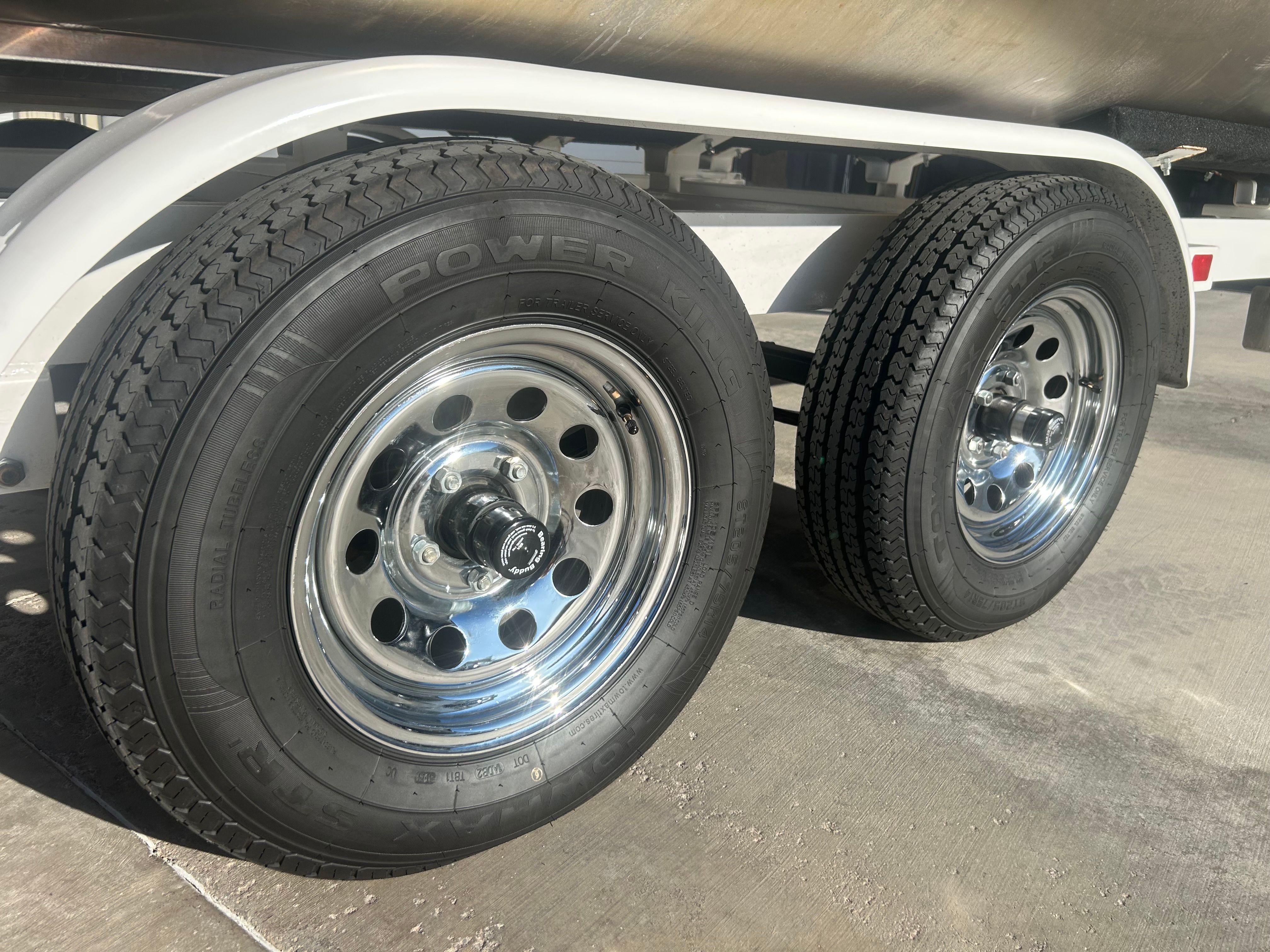 Close-up of two shiny, chrome trailer wheels on a concrete surface.
