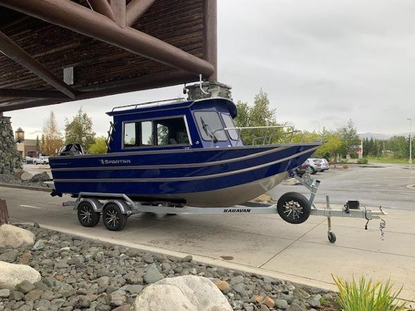 2023 Spartan 220 Maximus Pro boat on Karavan trailer, parked under wooden structure.