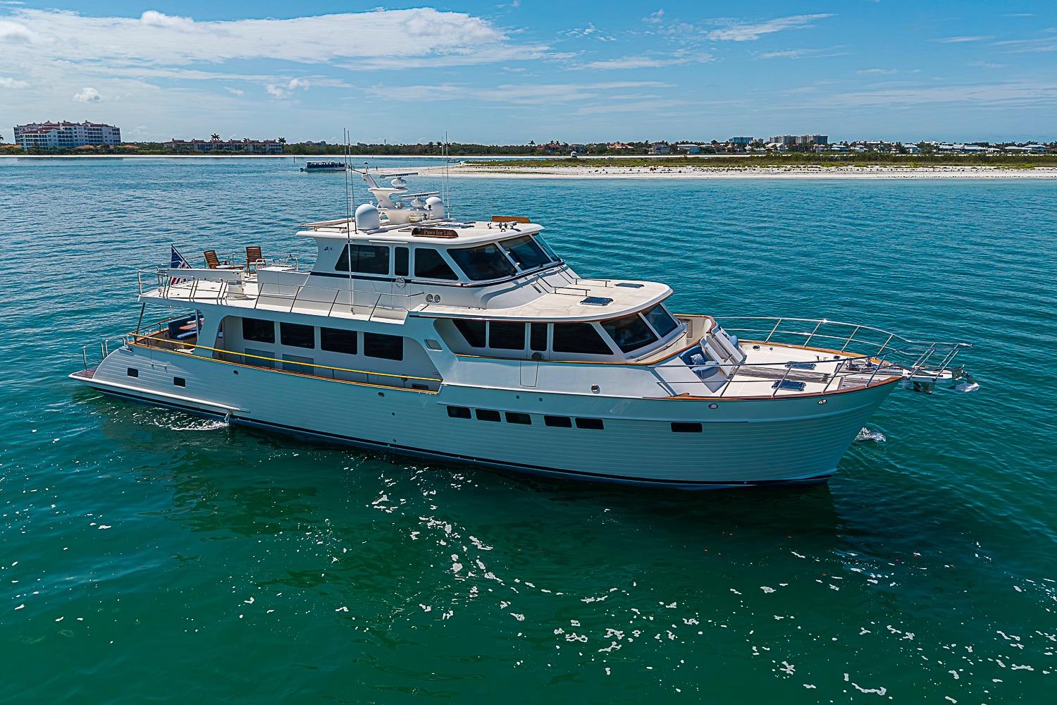 Luxurious 2014 Marlow 80 Explorer yacht cruising in clear blue waters near a scenic coastline.