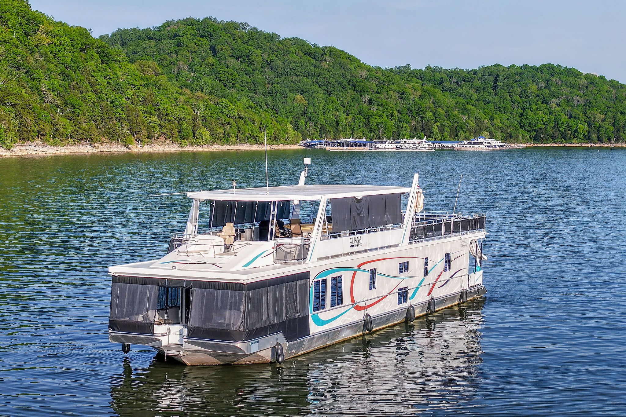 Houseboat on calm lake with forested backdrop, 2010 model.