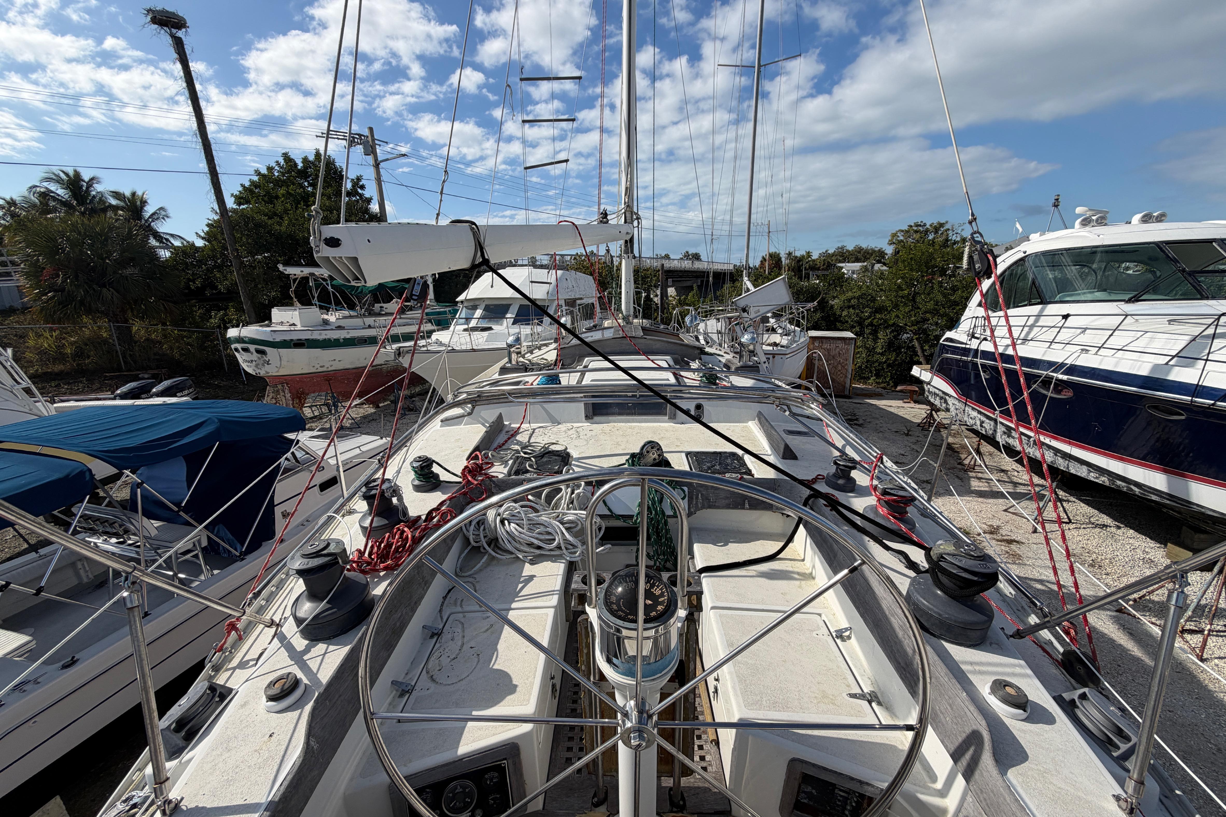 1983 Morgan Catilina sailboat deck with steering wheel, docked among other boats under a blue sky.