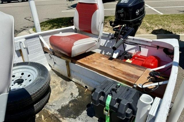 1958 Jon Boat Aluminum with red seats, outboard motor, and spare tire in parking lot.
