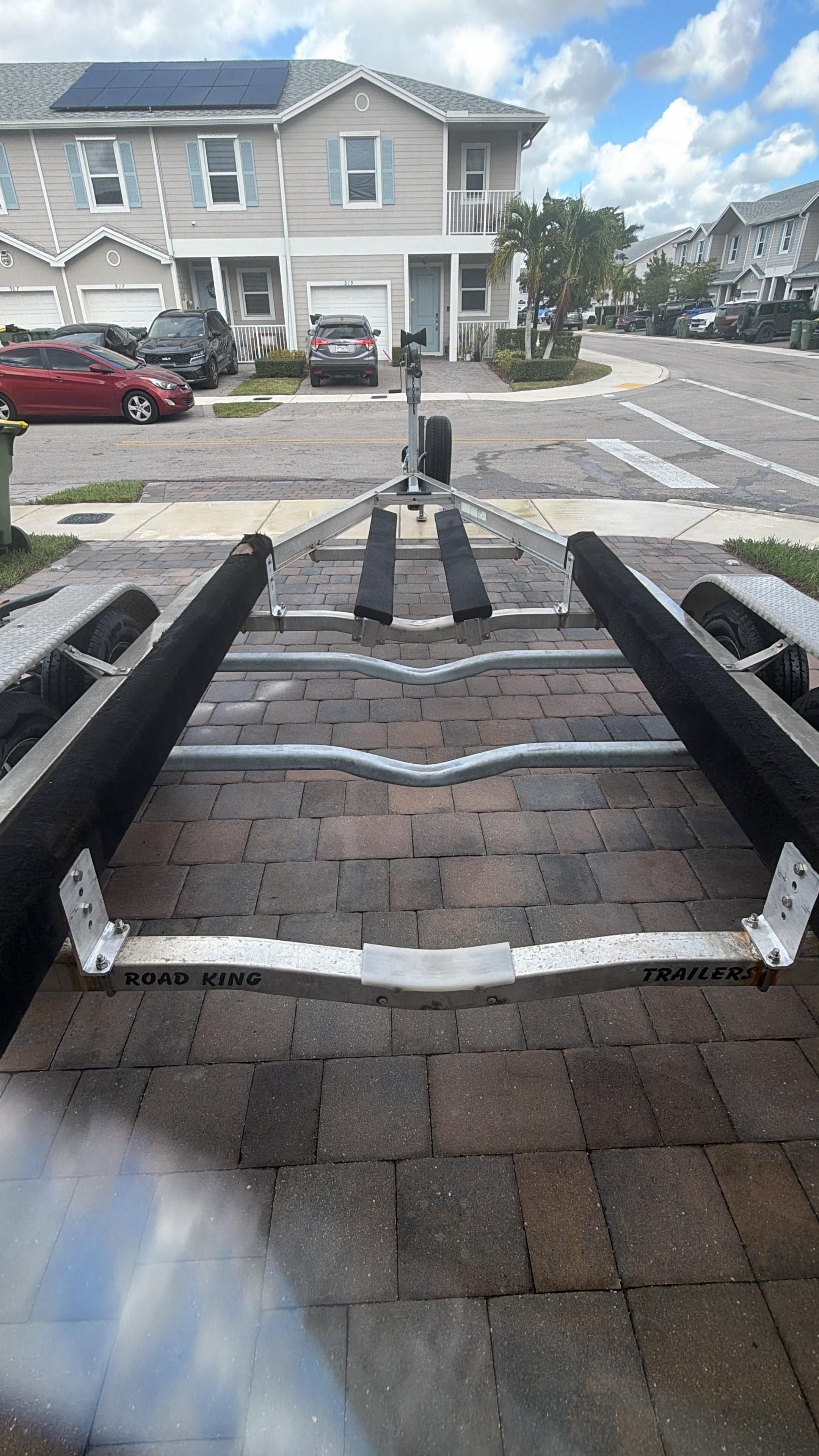 A boat trailer is parked on a paved driveway in a residential area.