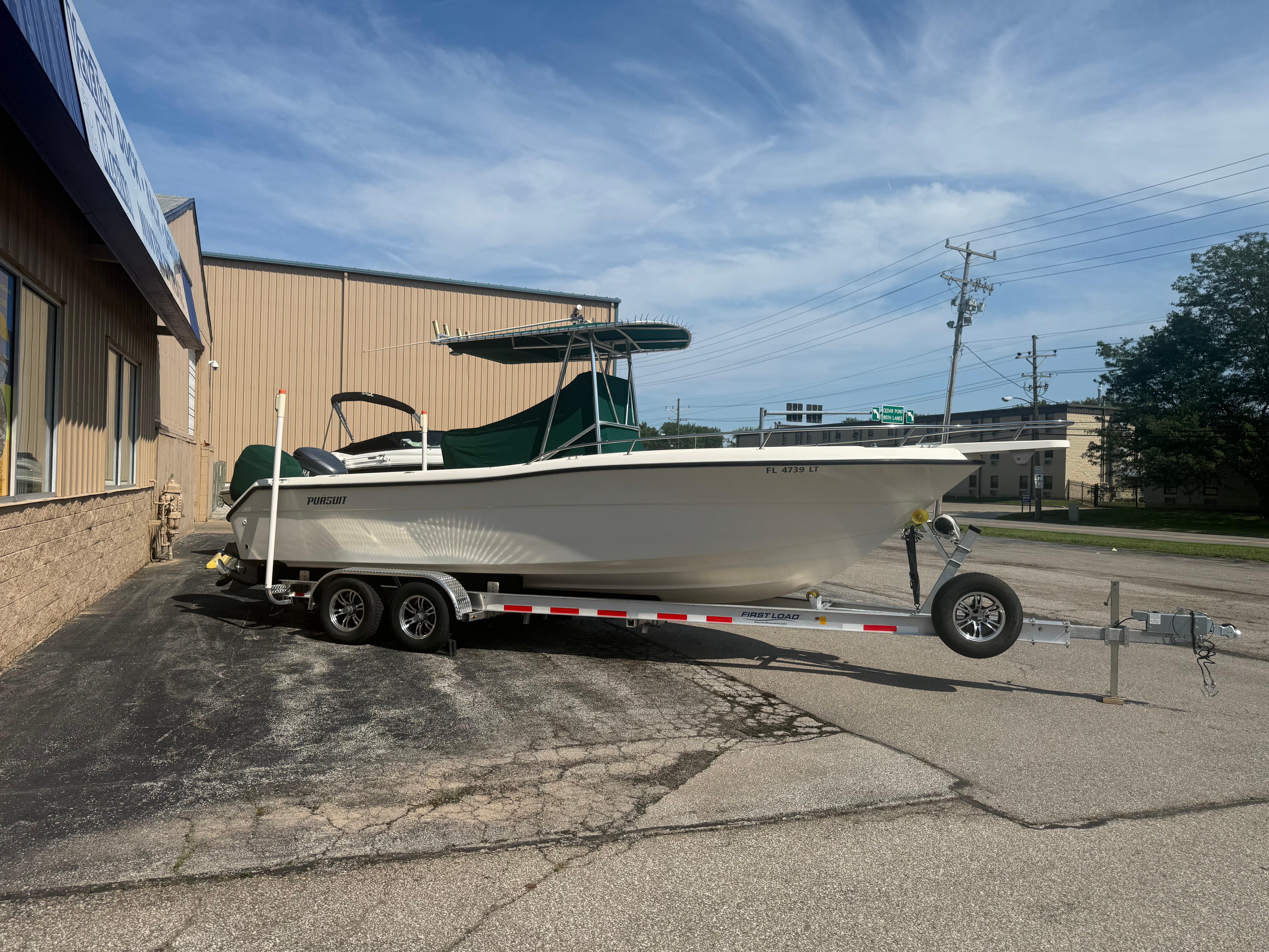 2002 Pursuit 2470 CC boat on trailer, parked outside a building under a clear sky.
