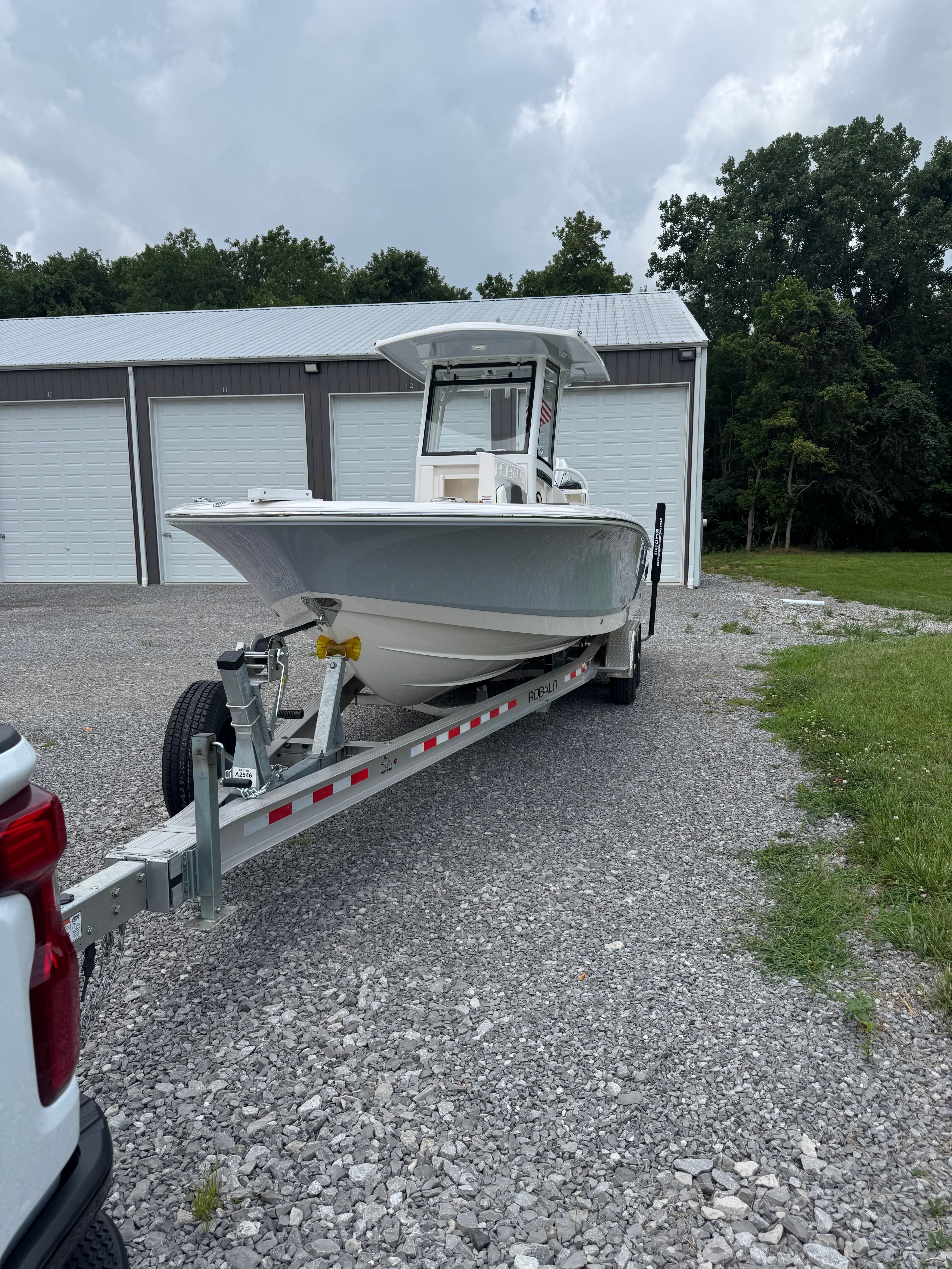 A 2023 Robalo 266 Cayman boat on a trailer in front of a garage.