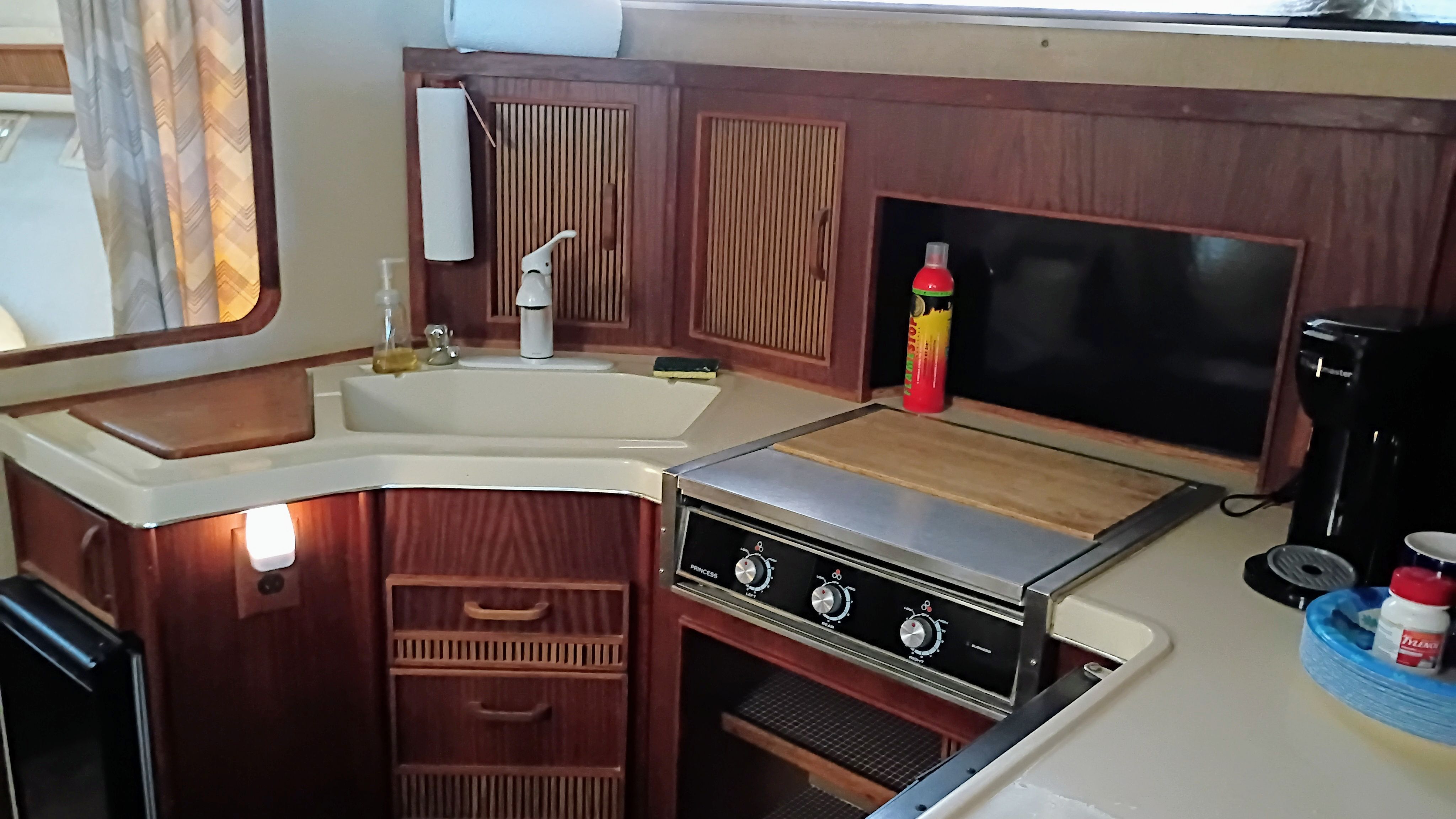 The galley of a 1986 Sea Ray Sundancer with wooden cabinets, stove, and sink.