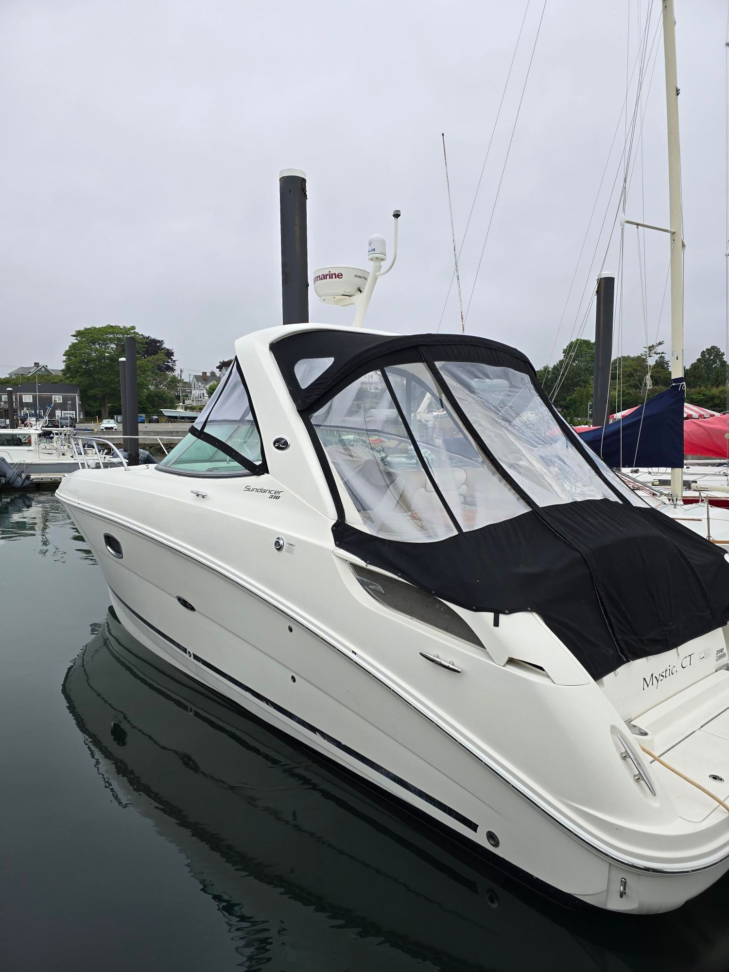A white Sea Ray Sundancer 310 boat docked in a harbor, surrounded by other boats.