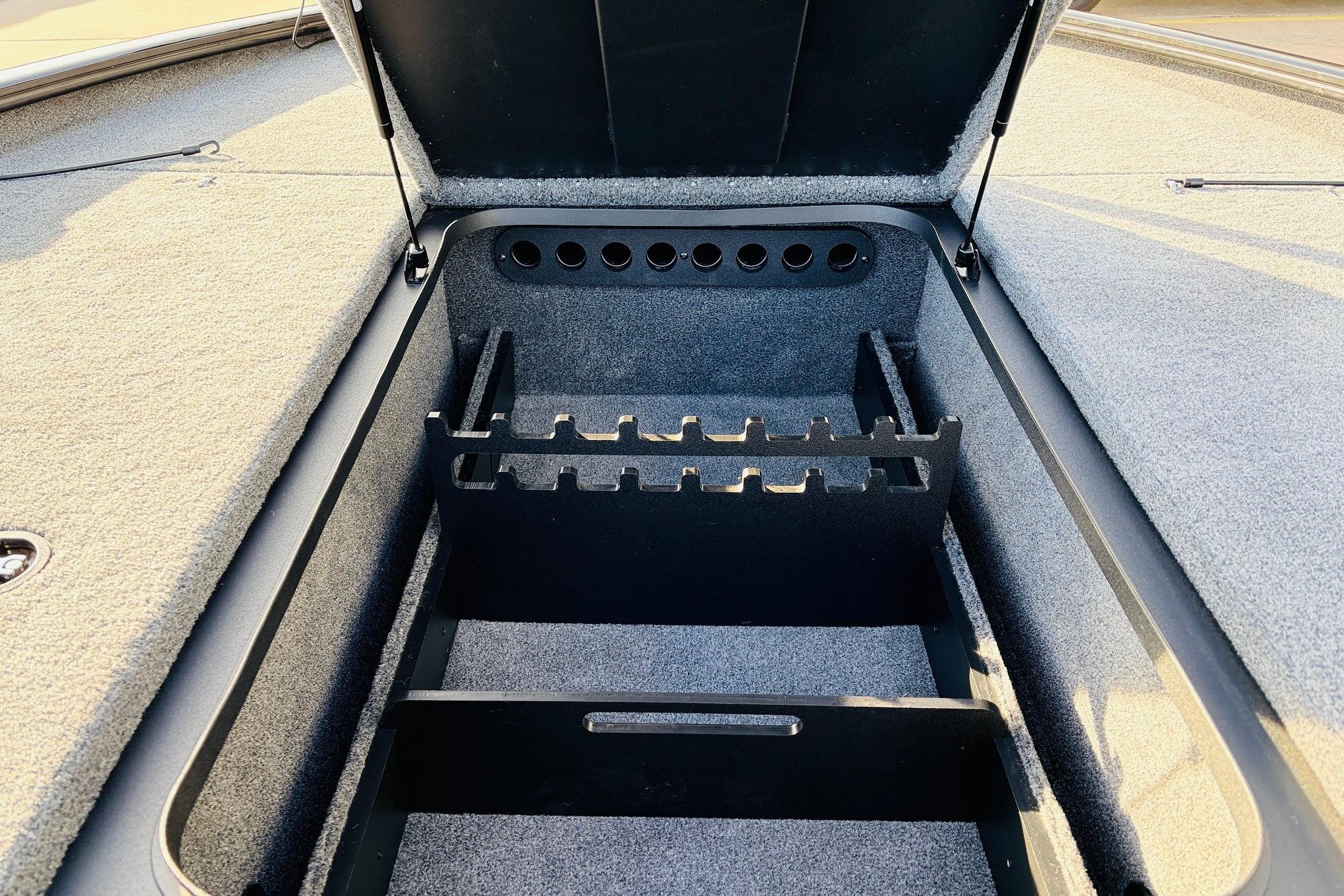 Open storage compartment in 2025 Tracker Savage 215 boat, featuring rod holders and carpeted interior.