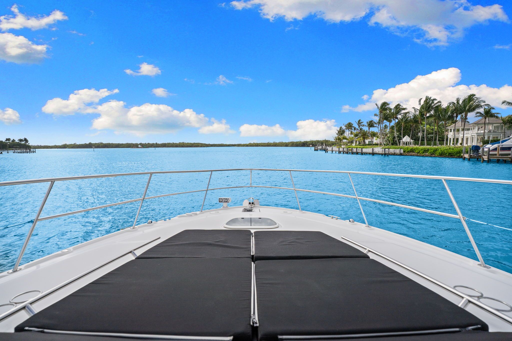 View from the bow of a Sea Ray Sundancer 510 over calm blue water and palm trees onshore.