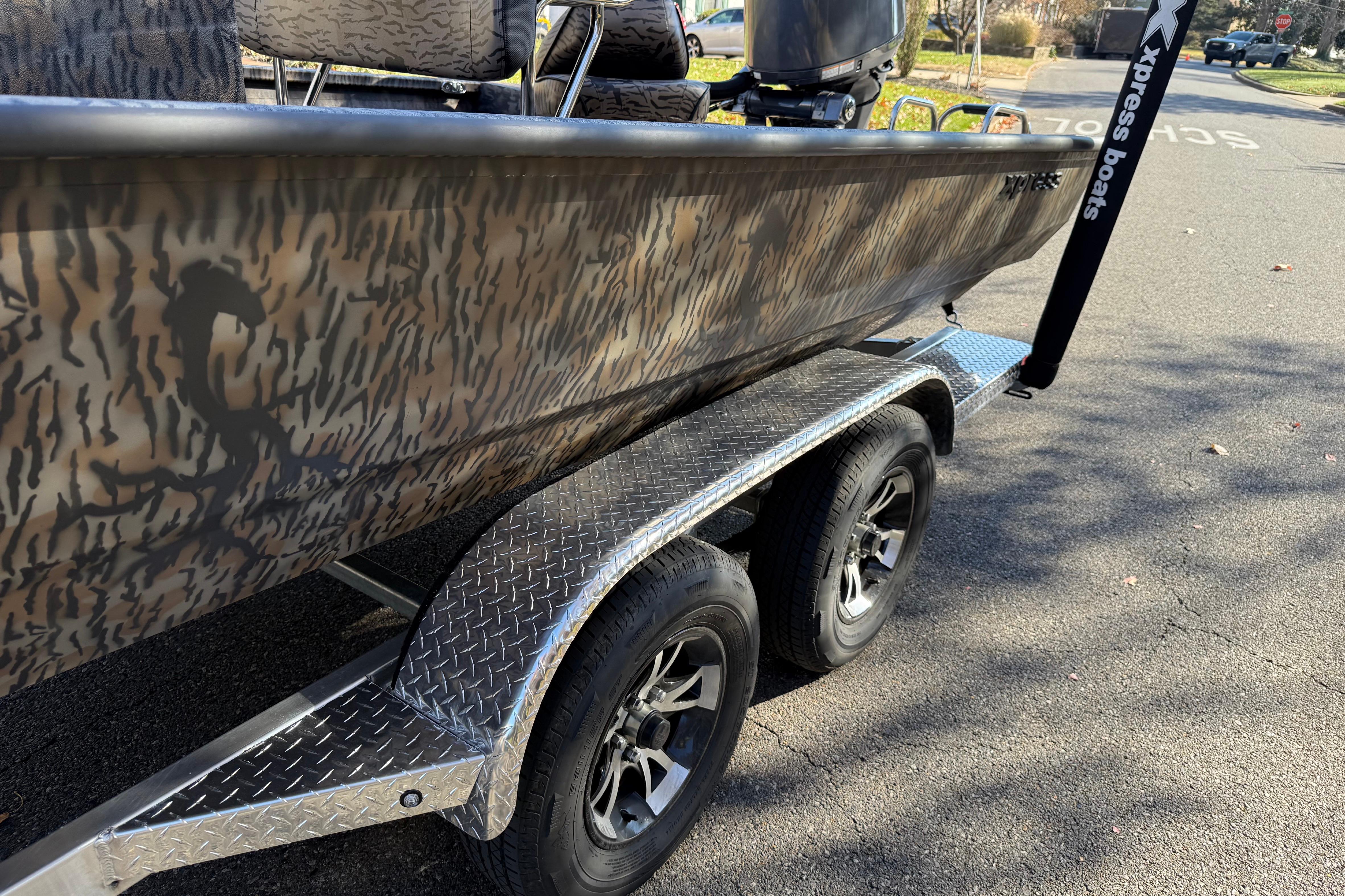 2025 Xpress H22B Bay boat on trailer with camouflage design and dual wheels.