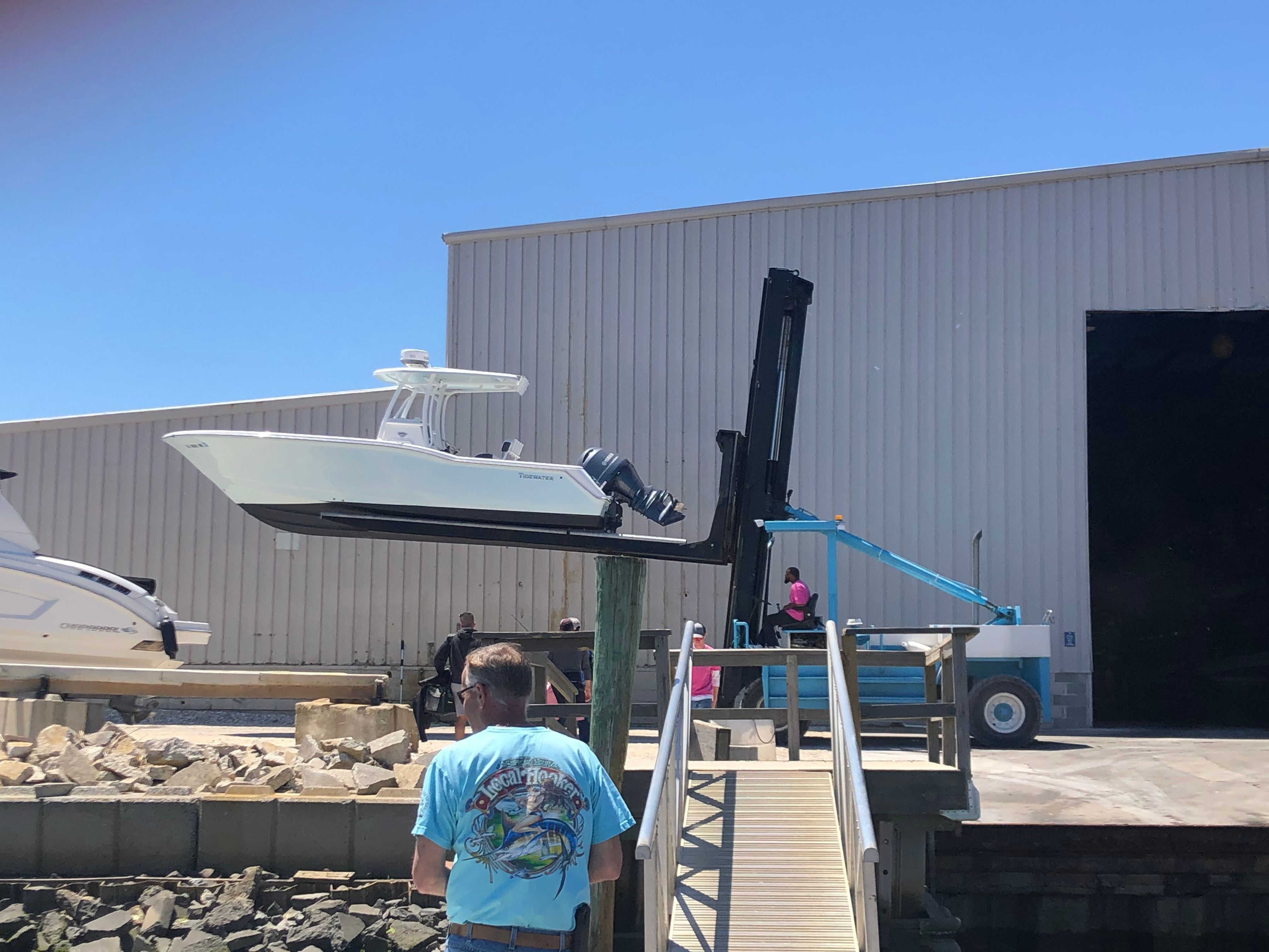 A white boat is being lifted by a forklift from a warehouse.