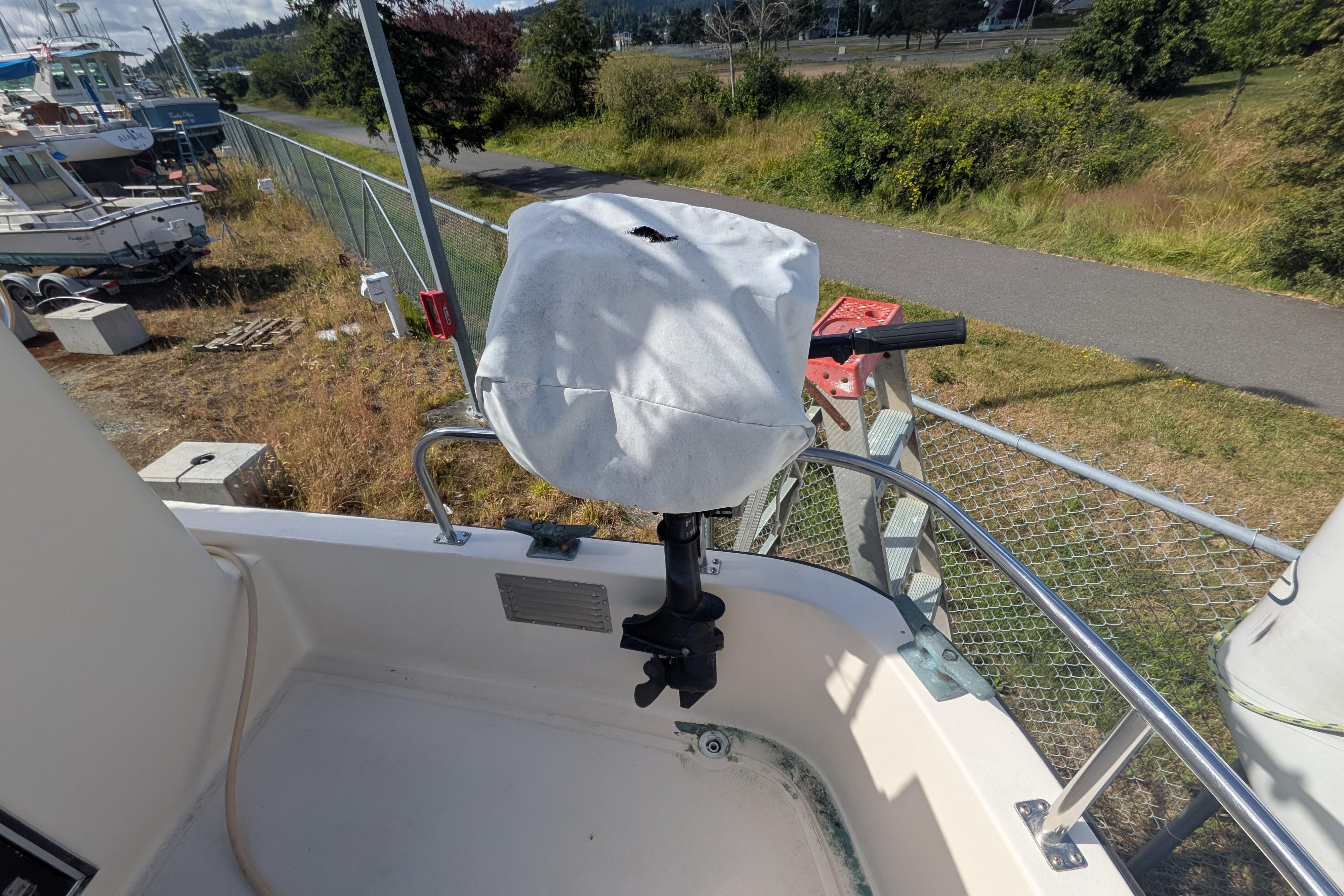Covered outboard motor on a 1998 Nordic Tug 32, docked near a grassy area.