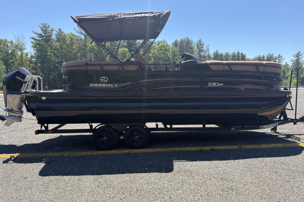 2026 Regency 230 DL pontoon boat on trailer, parked outdoors with trees in background.