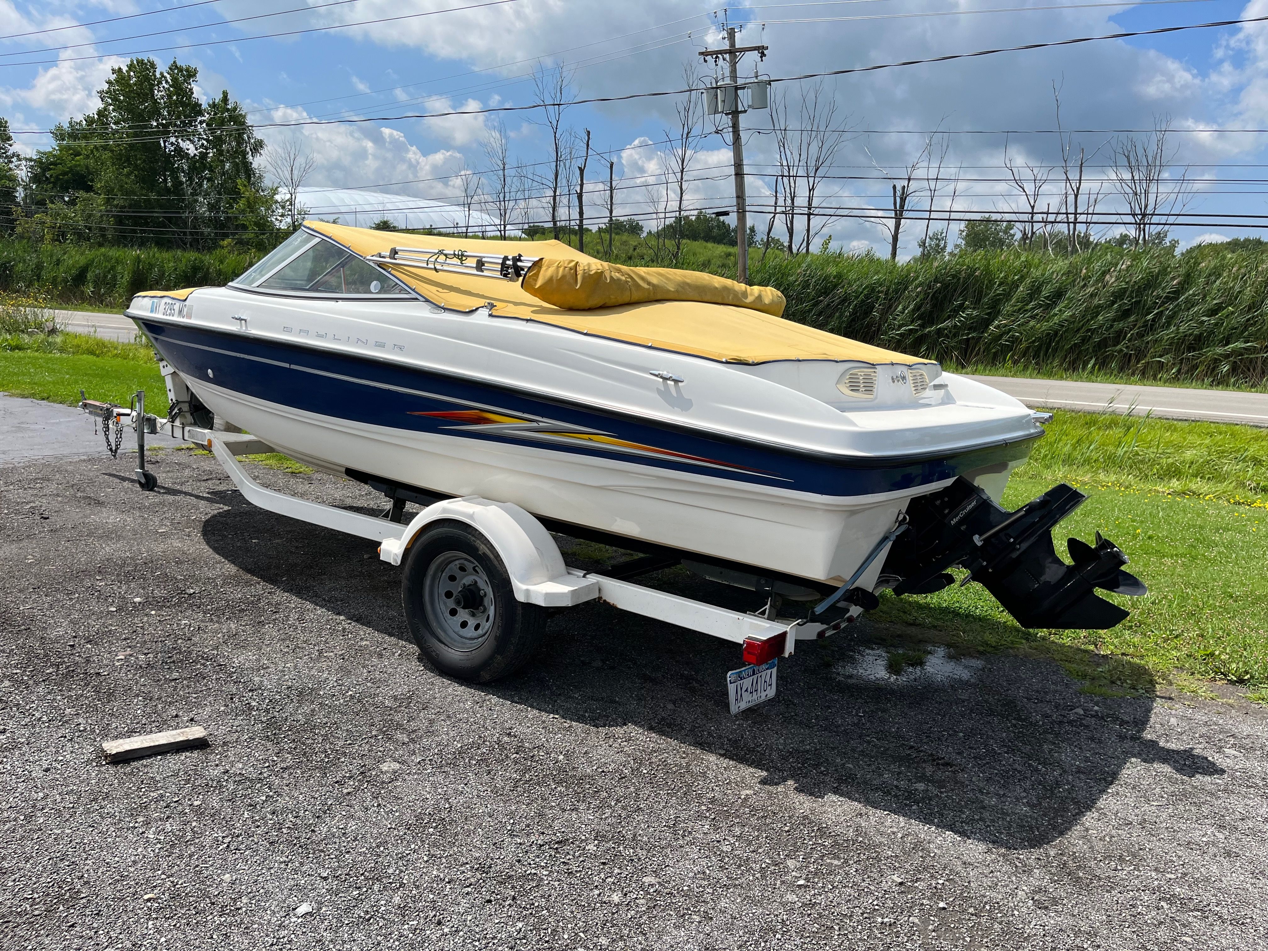 A 2005 Bayliner 205BR on a trailer, with a yellow cover, parked on a lot.