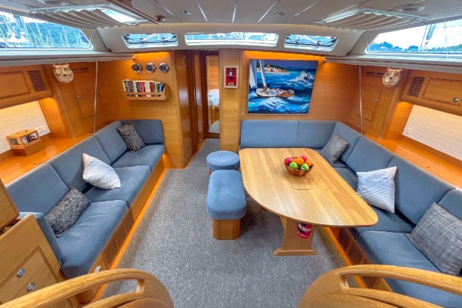 Luxurious 2020 Hallberg-Rassy 57 yacht interior with cozy seating and elegant wooden table.