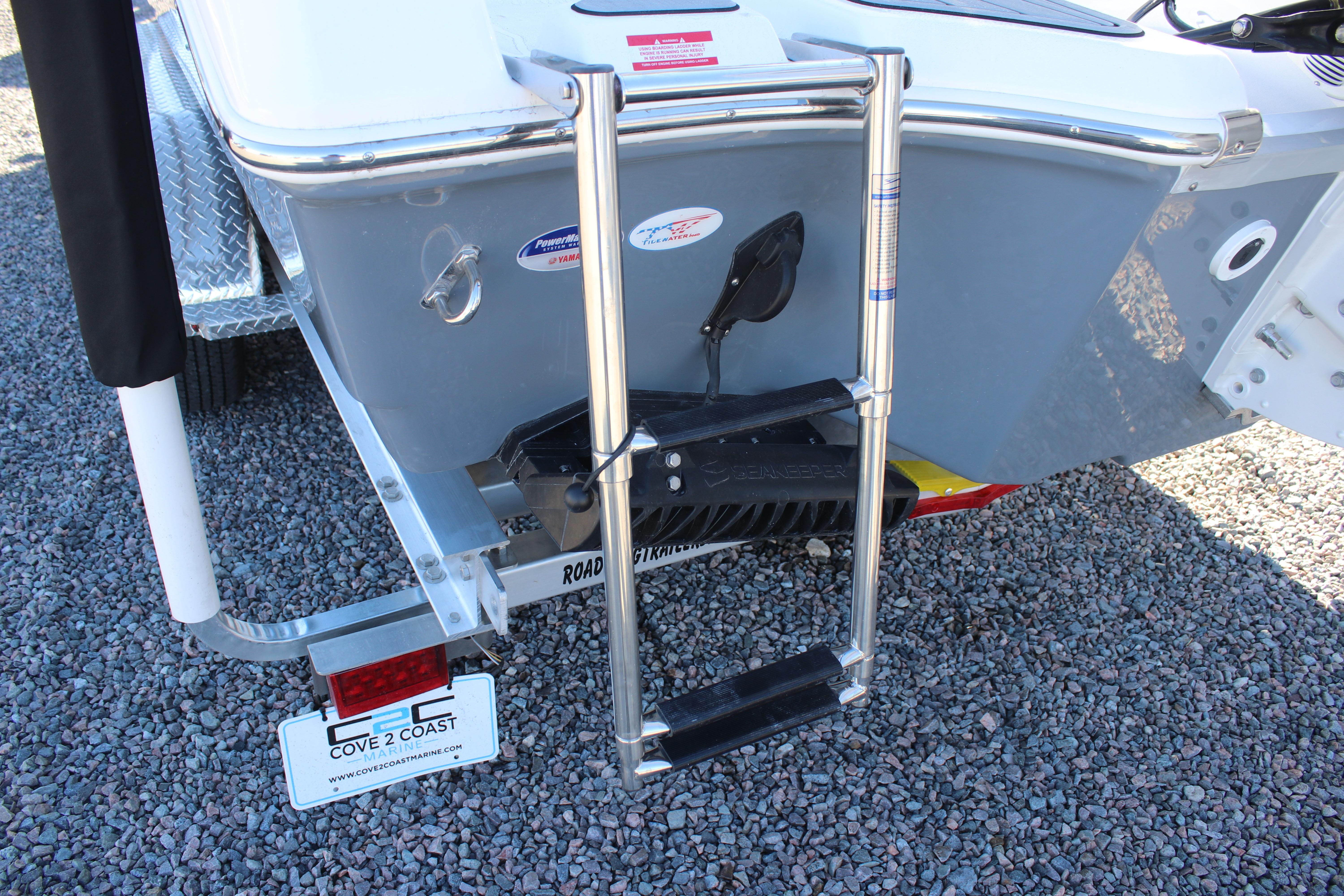 2026 Tidewater 232 CC Adventure boat with ladder and trailer on gravel surface.