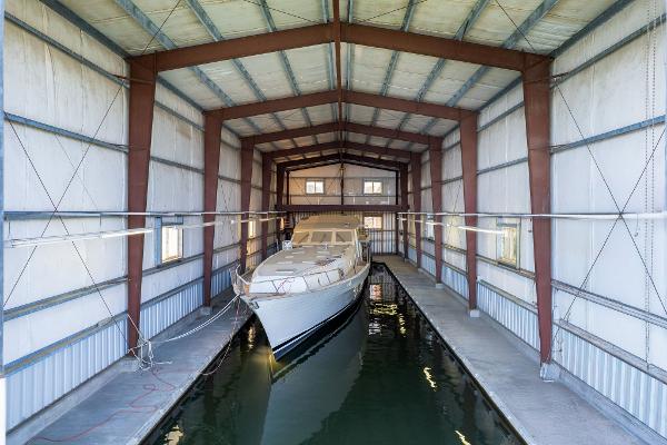 A 1985 Custom Larson Boathouse with a yacht docked inside, featuring metal beams and waterway.