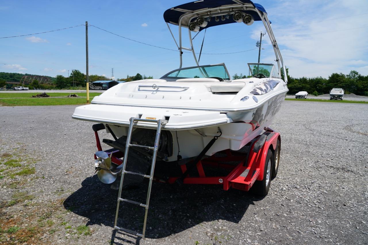 2004 Crownline 216 LS boat on red trailer, featuring swim ladder and canopy, parked outdoors.