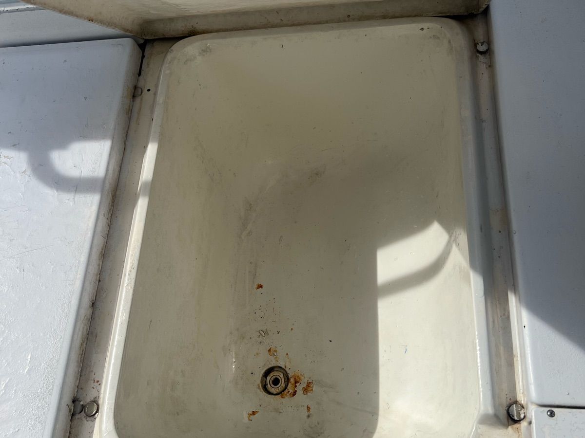 An empty, rectangular storage compartment on a boat with a drain in the center.