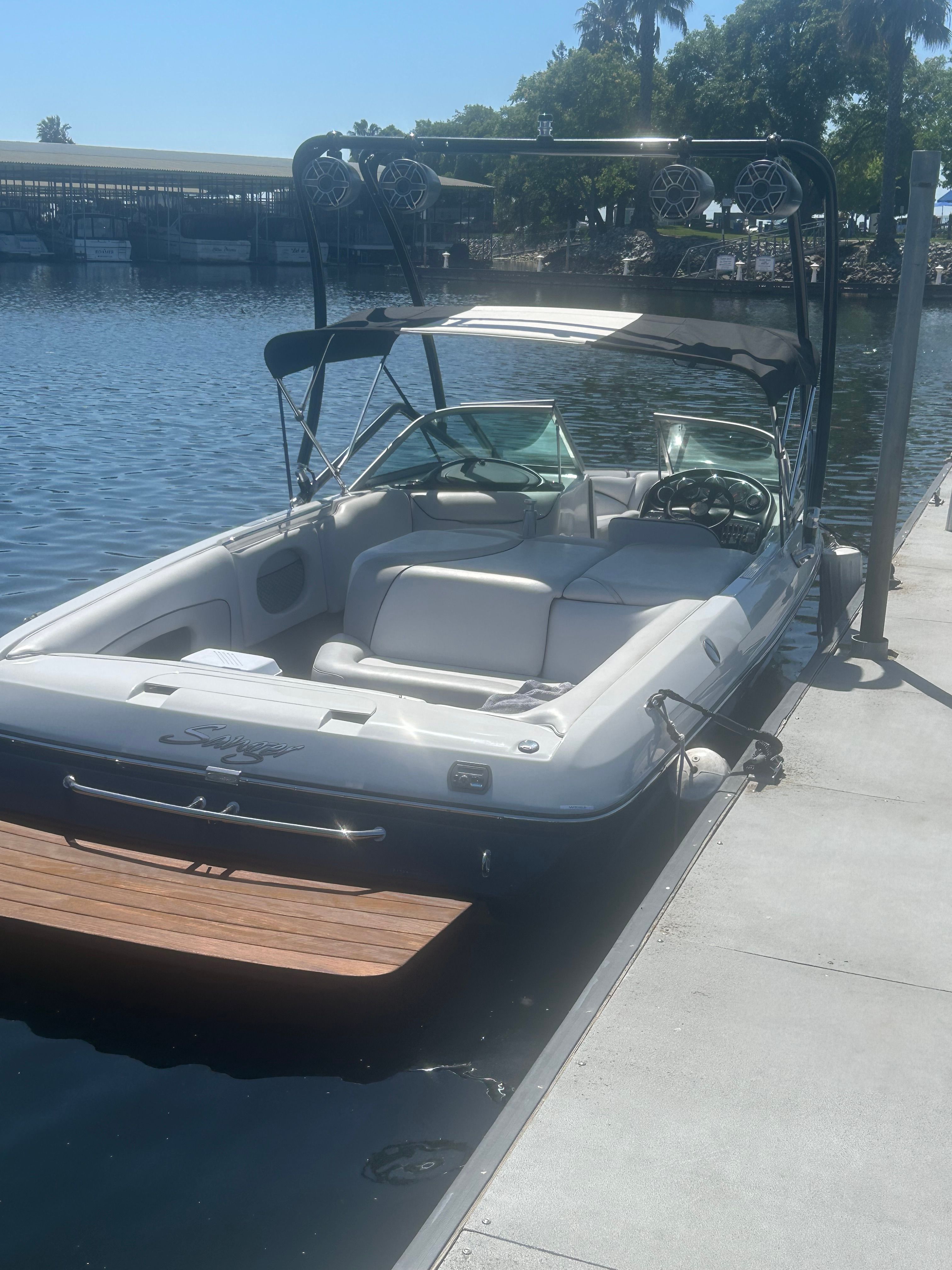 A white motorboat docked at a pier, surrounded by calm water and trees.