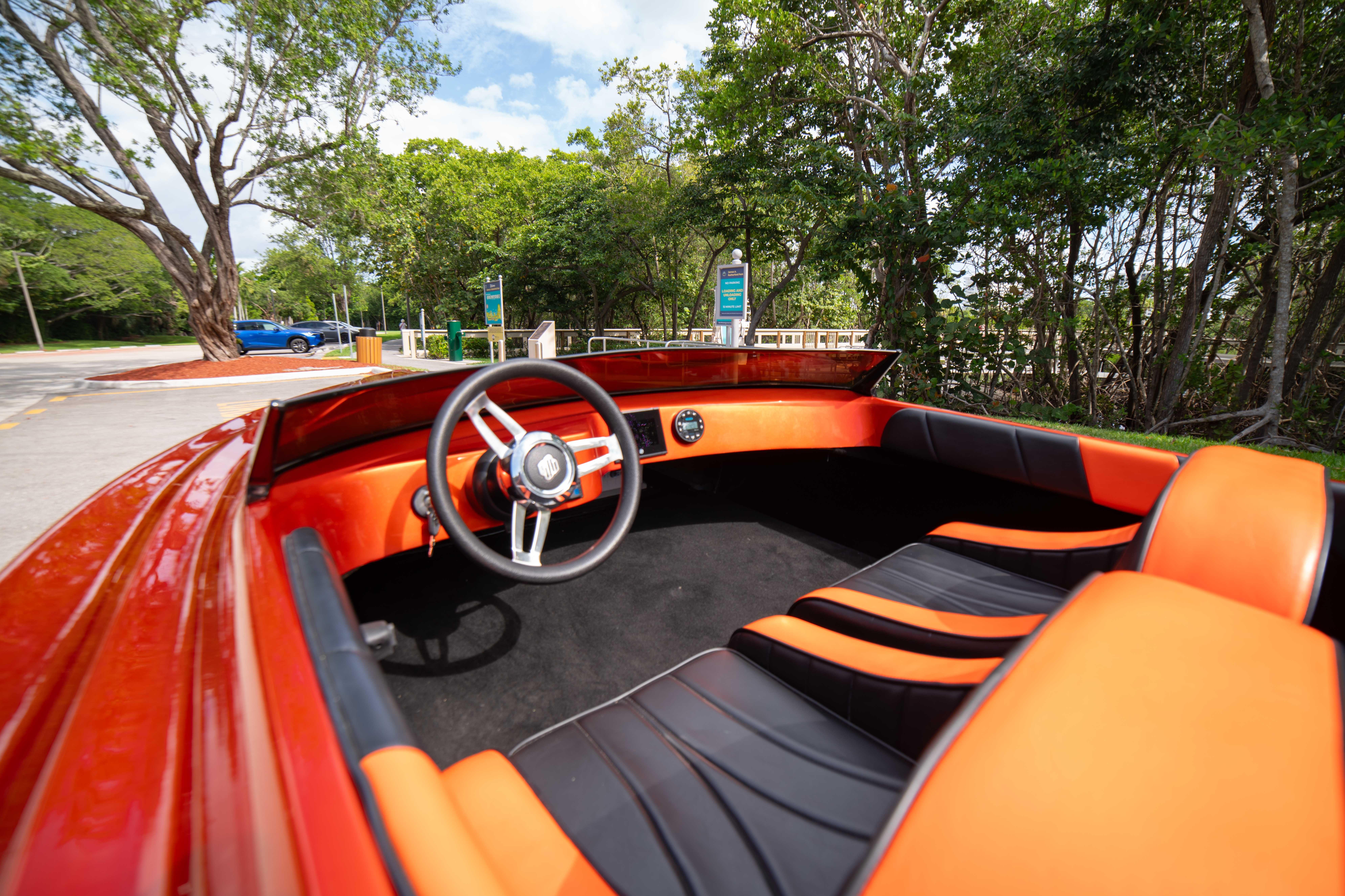 1984 Sleekcraft Aristocrat 20 boat interior with orange and black seating, parked near trees.