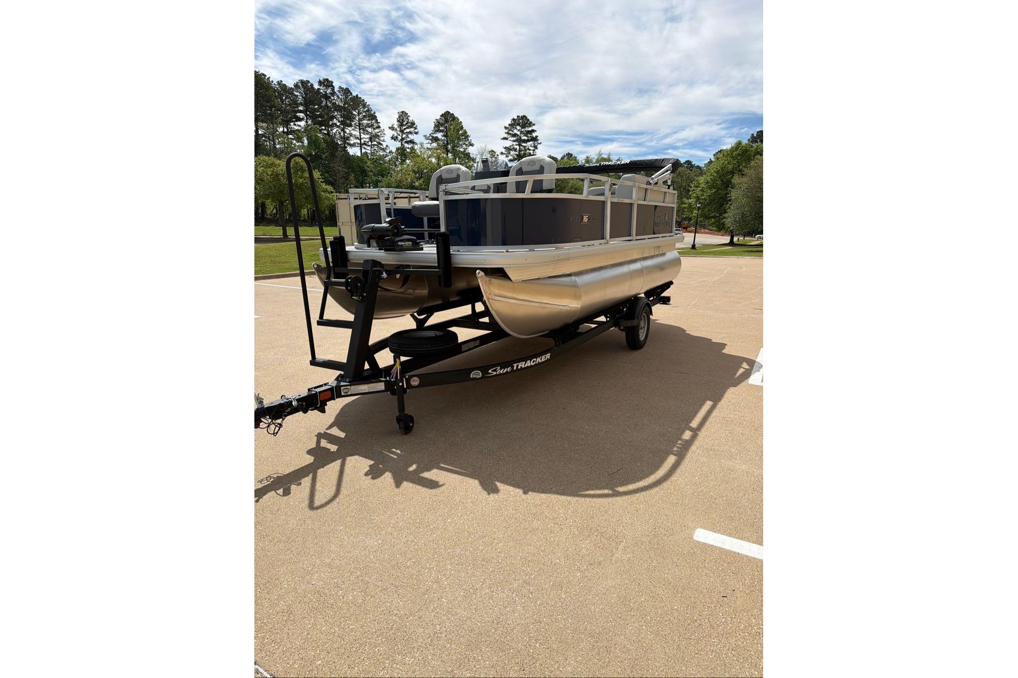 2026 Sun Tracker Bass Buggy 16 XL Select pontoon boat on trailer in parking lot.