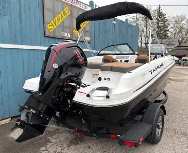 2025 Tahoe 185 S boat with outboard motor on trailer, parked near blue building.