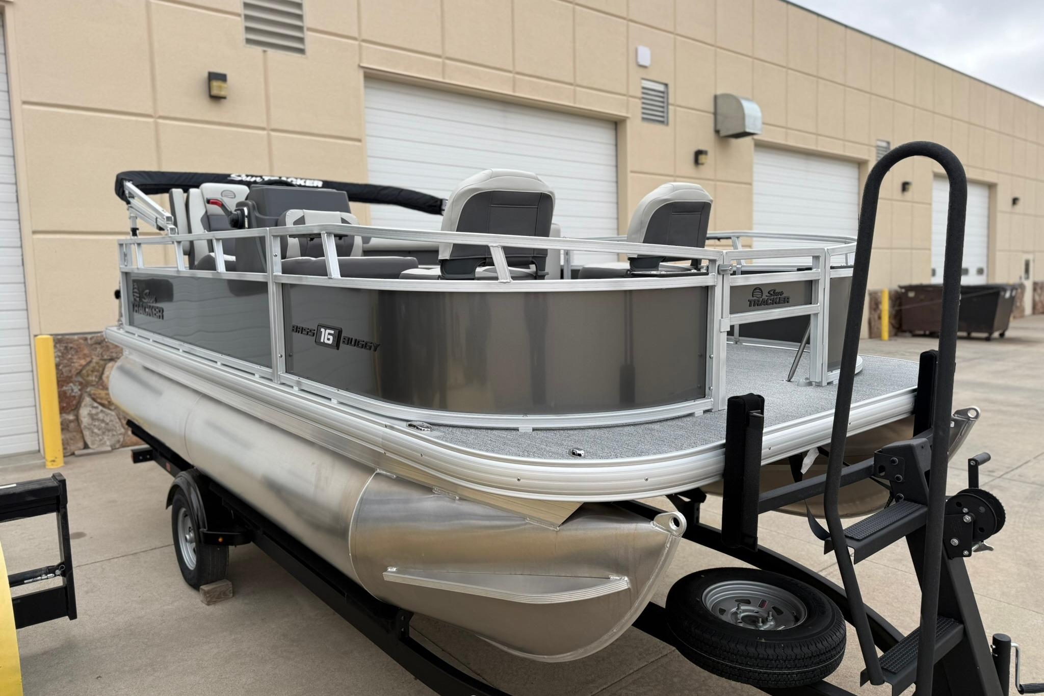 2026 Sun Tracker Bass Buggy 16 XL Select pontoon boat on trailer, parked outdoors.