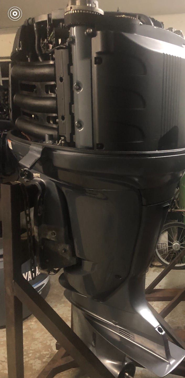 An outboard motor in a workshop, mounted on a stand. It is dark gray and sturdy.
