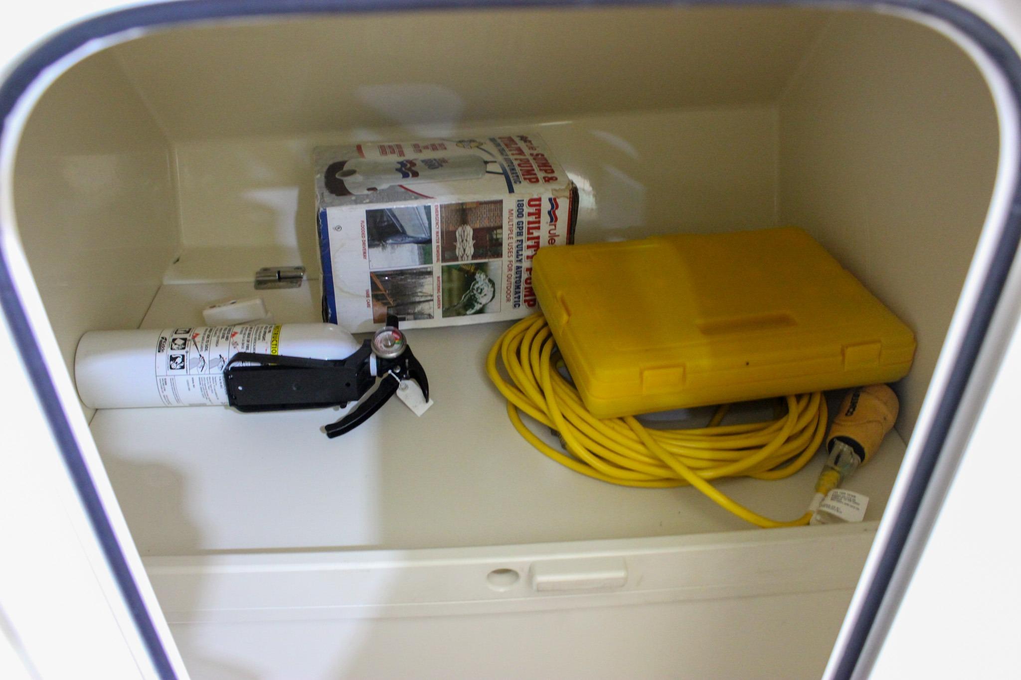 Storage compartment in 2018 Chris-Craft Calypso 30 with fire extinguisher, yellow cable, and utility pump.