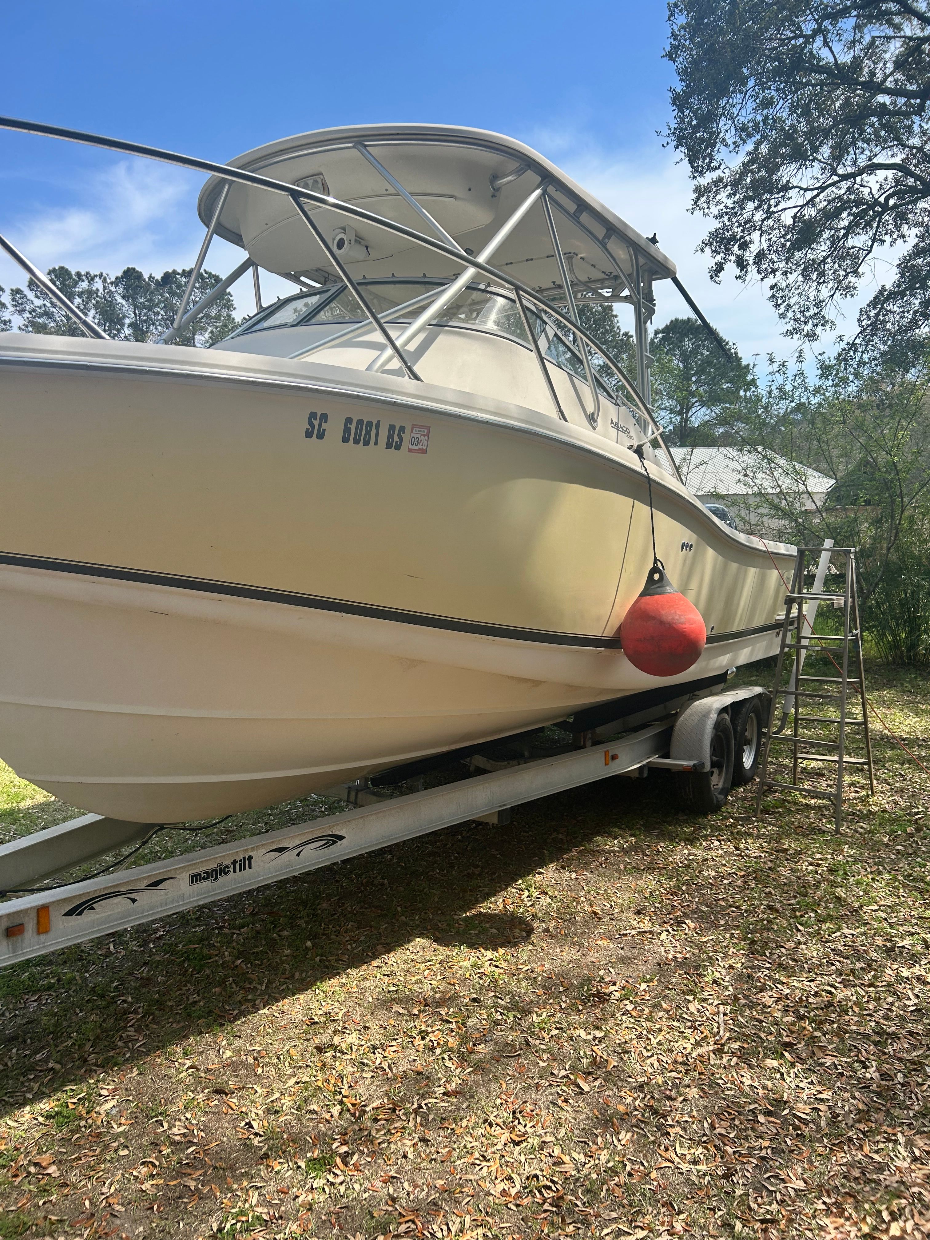 A 2003 Scout 280 Abaco boat on a trailer, surrounded by trees.