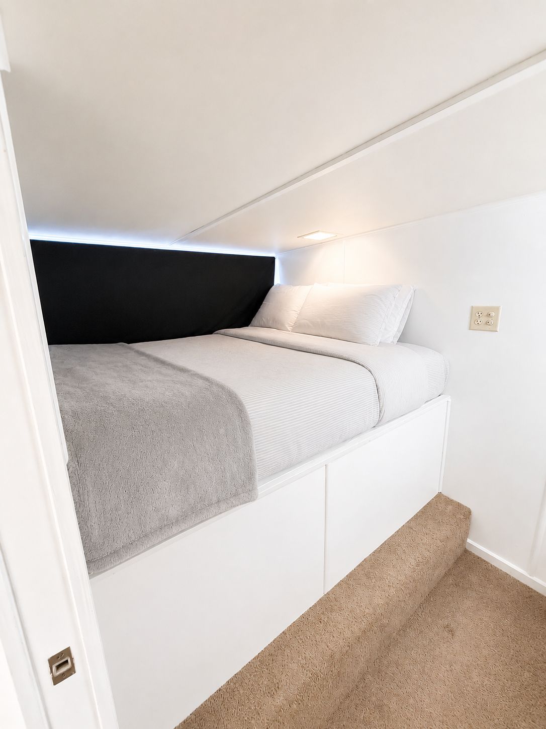 A cozy bedroom with a bed built into a corner and carpeted flooring.