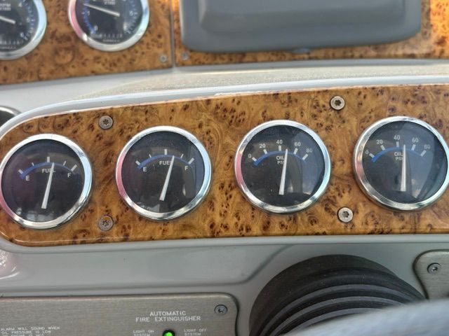 Close-up of four round gauges on a boat, surrounded by wood paneling.
